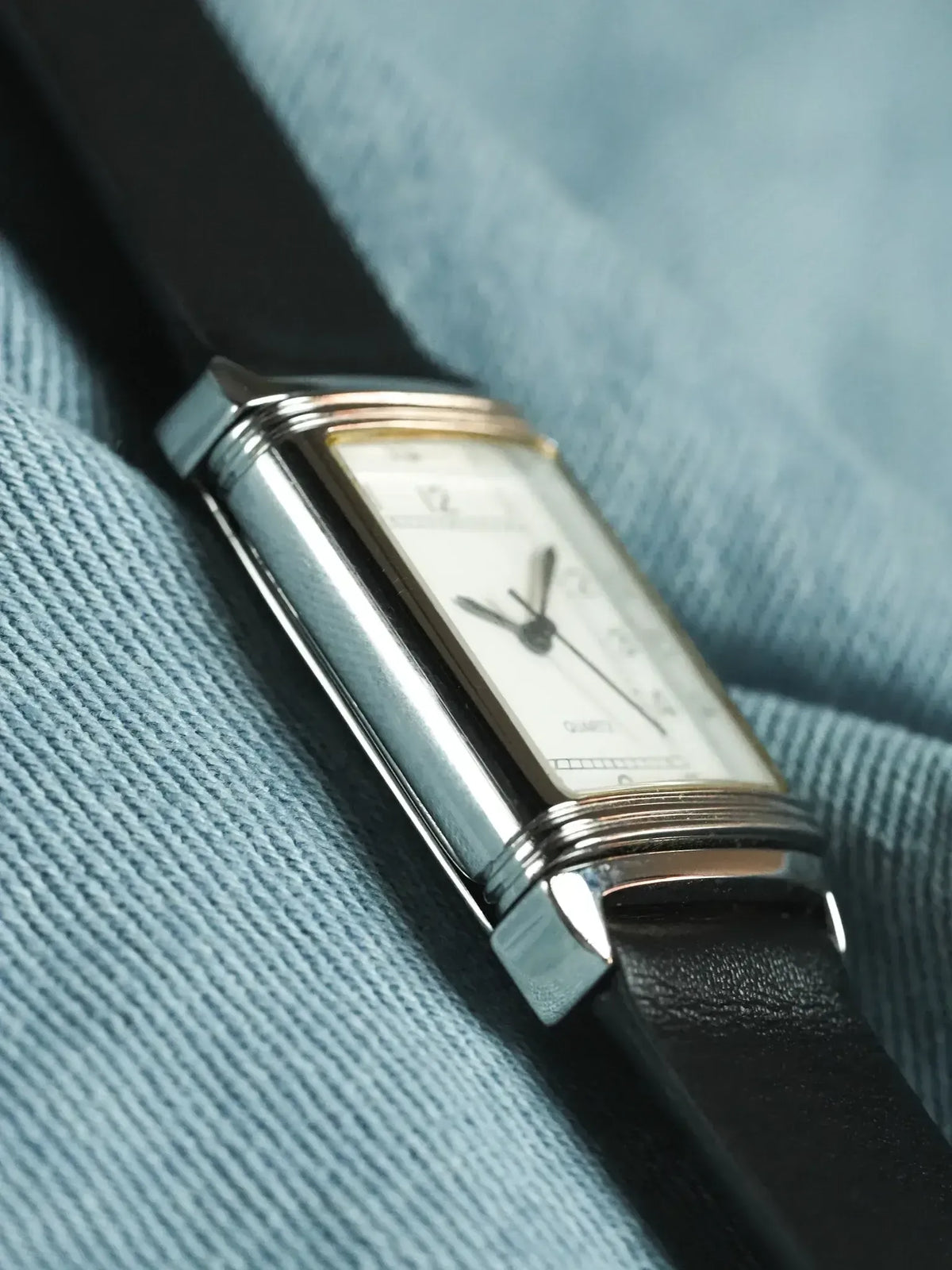 Cartier Tank vintage watch with white dial, gold accents, black leather strap on blue fabric
