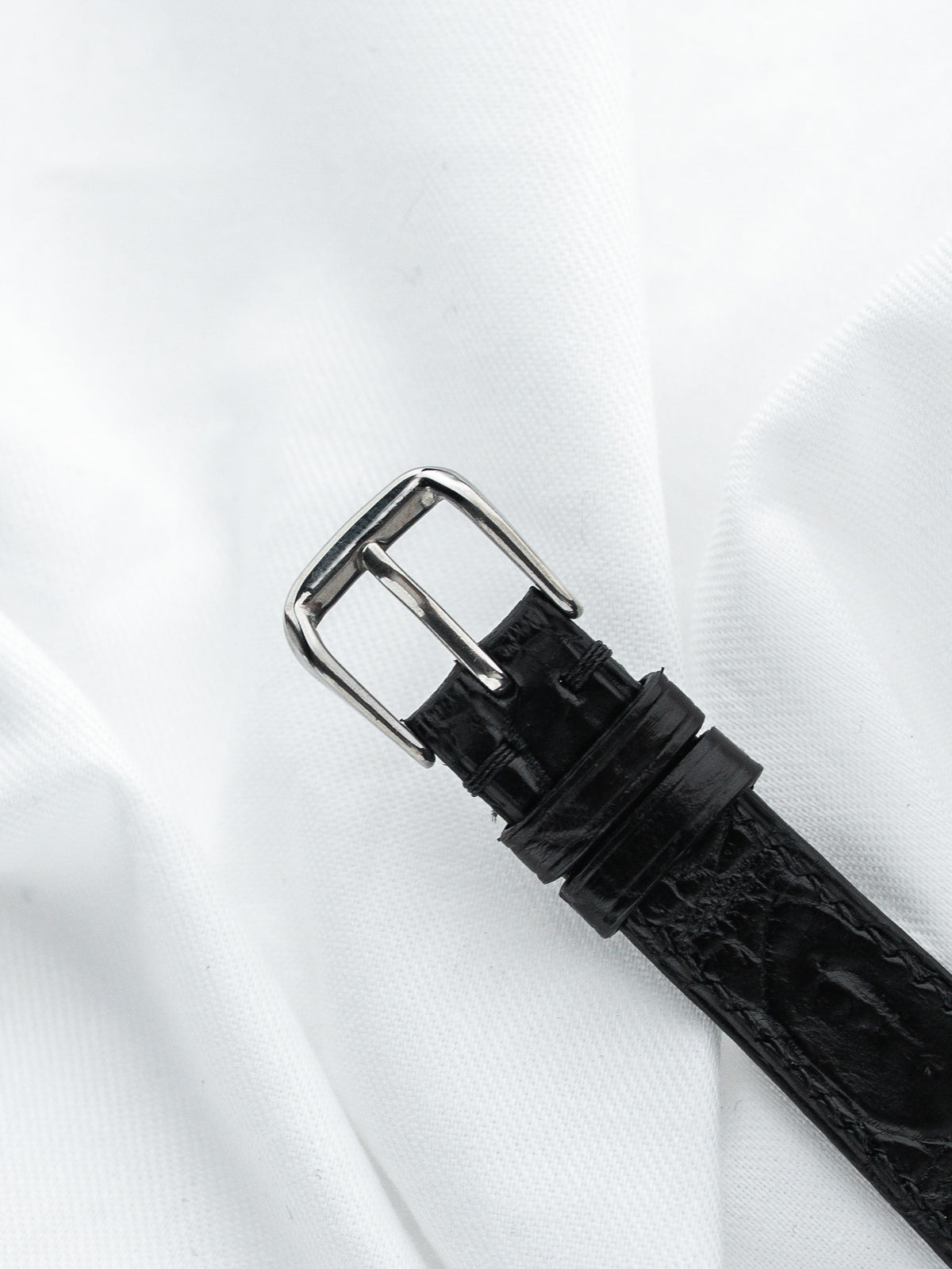 Bracelet de montre en cuir noir effet crocodile avec boucle argentée sur fond blanc