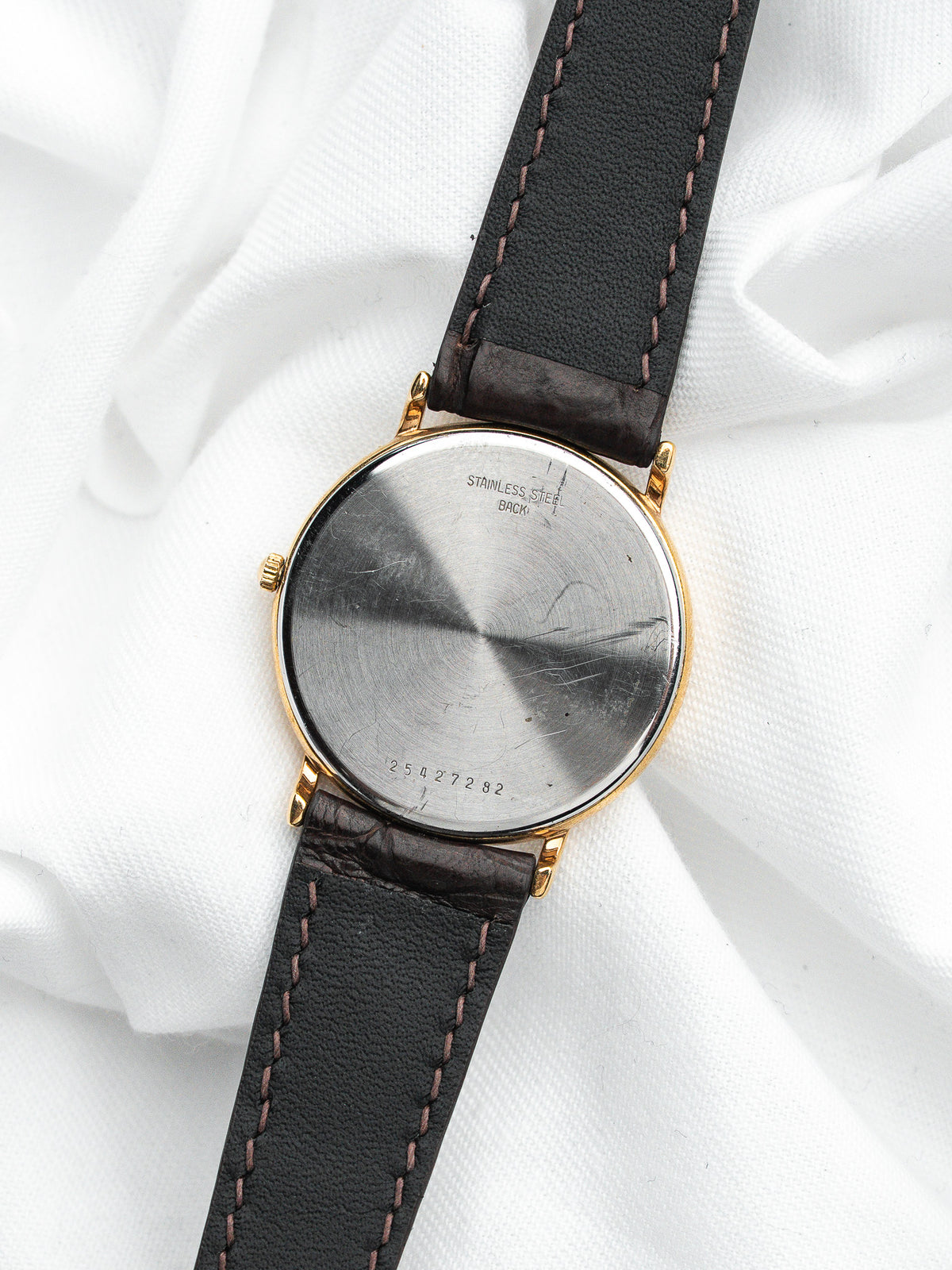 Dos d'une montre vintage avec boîtier doré et bracelet en cuir noir sur tissu blanc