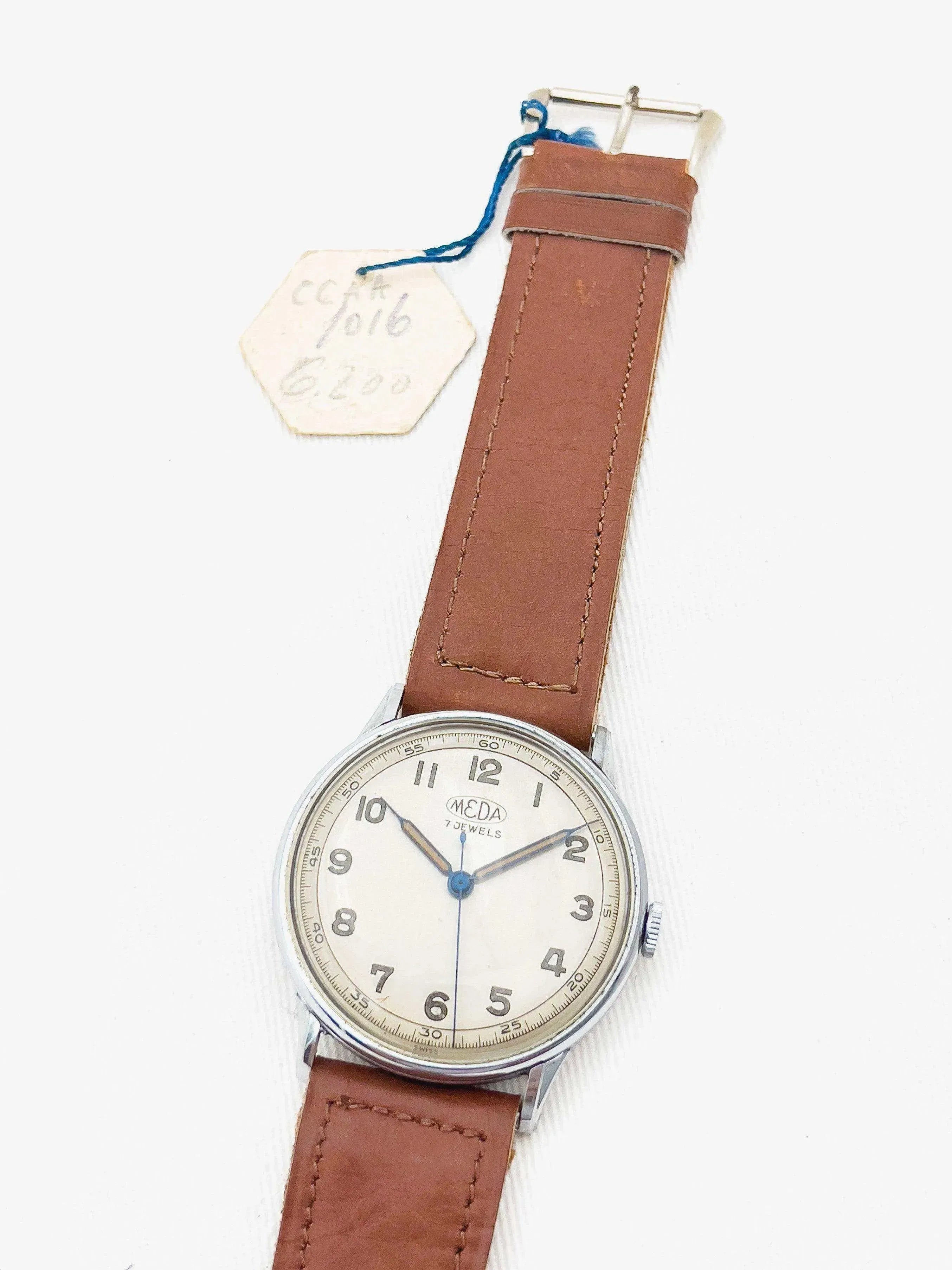Meda vintage watch with cream dial, brown leather strap, and blue hands on white background