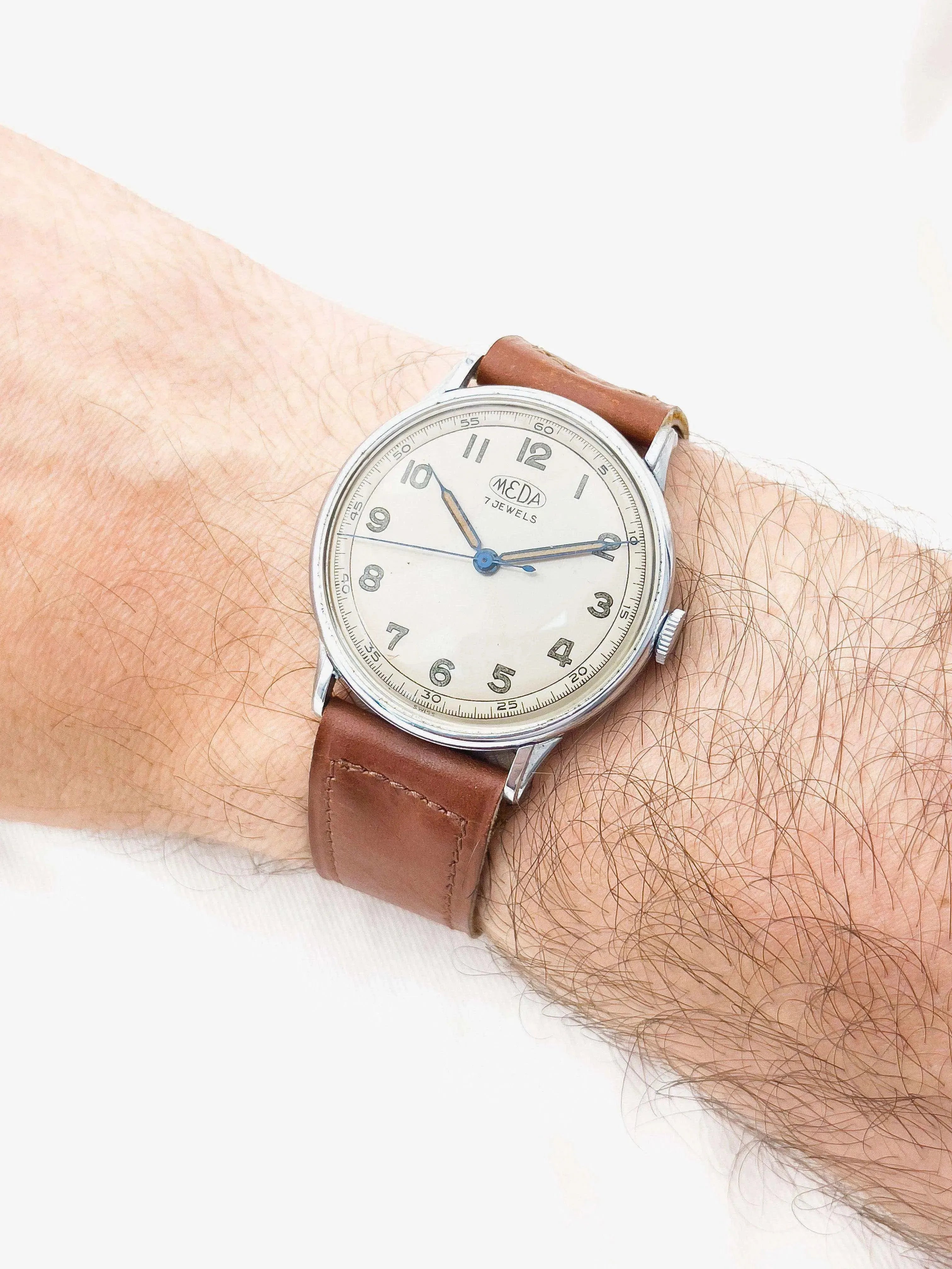 Vintage Meda watch with cream dial, blue hands, brown leather strap worn on wrist