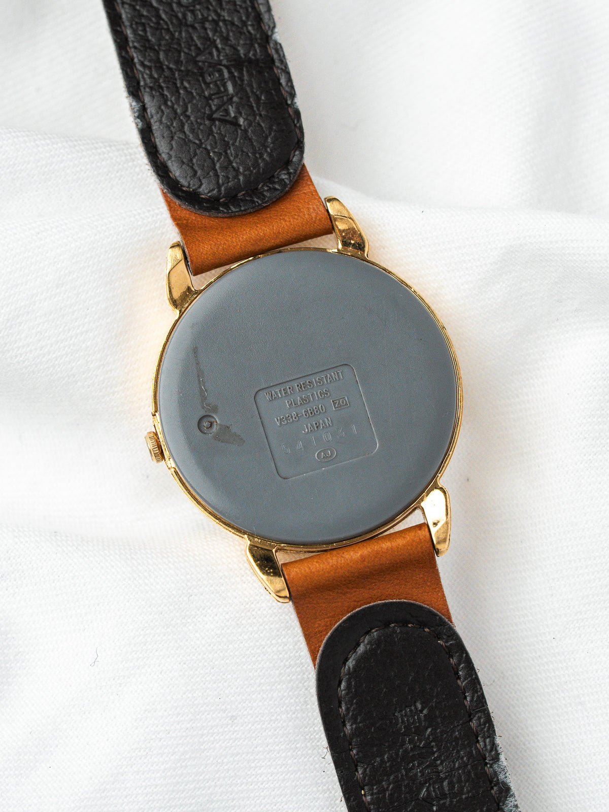 Vintage Seiko watch with gold case, brown leather strap, and engraved case back on white fabric