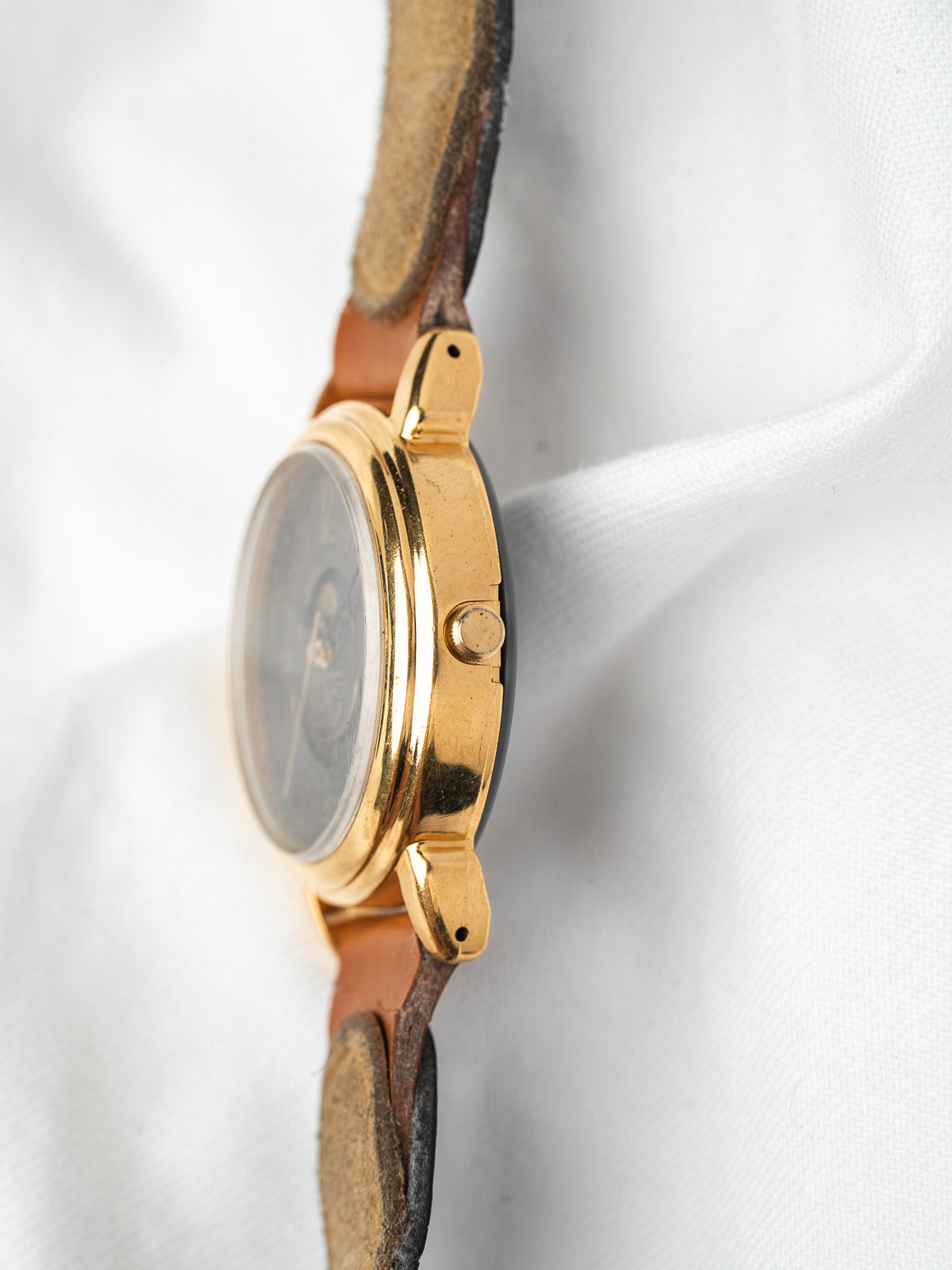 Vintage gold watch with brown leather strap on white fabric