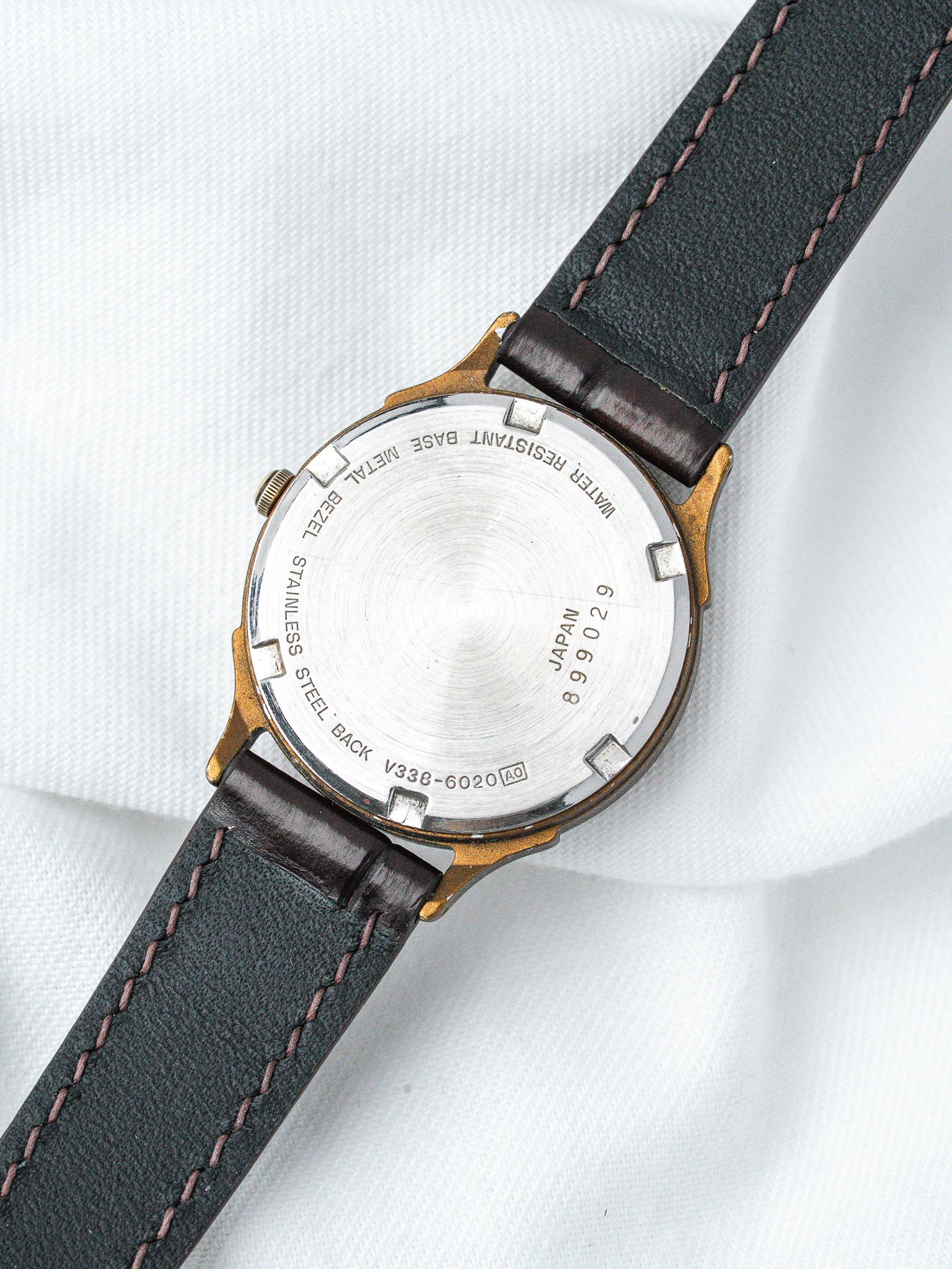 Vintage Seiko watch with stainless steel back, gold-tone case, black leather strap on white fabric