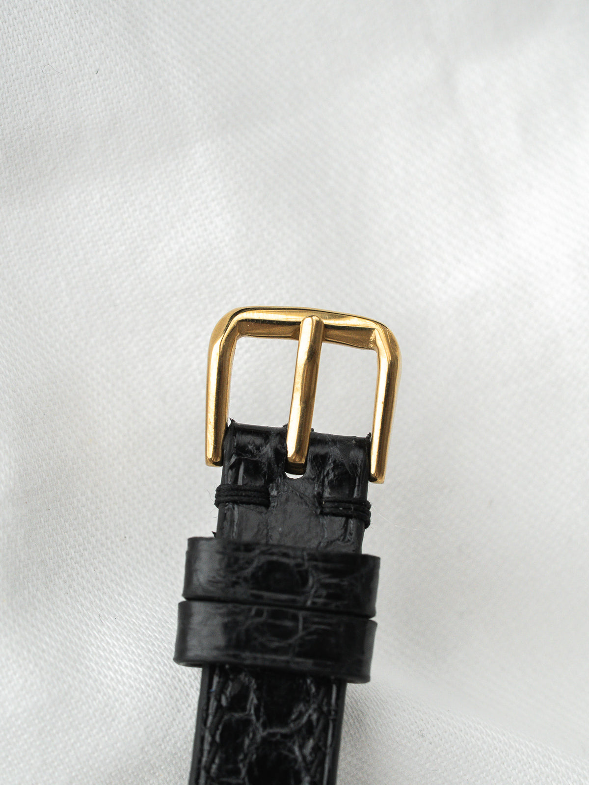 Boucle de bracelet de montre en or avec cuir noir grainé sur fond blanc