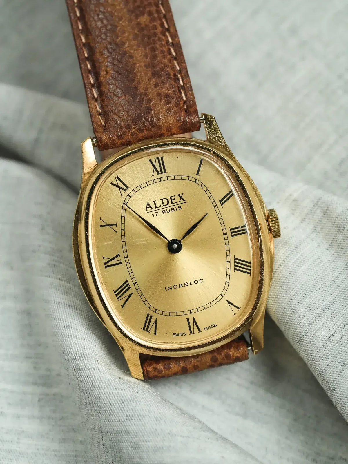 Vintage Aldex watch with gold case, cream dial, Roman numerals, and brown leather strap