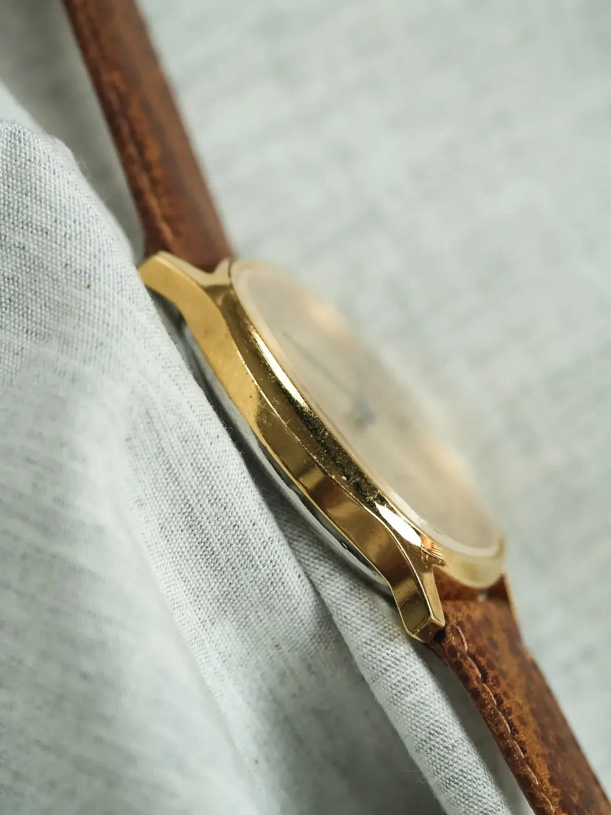 Vintage gold watch with brown leather strap resting on light fabric