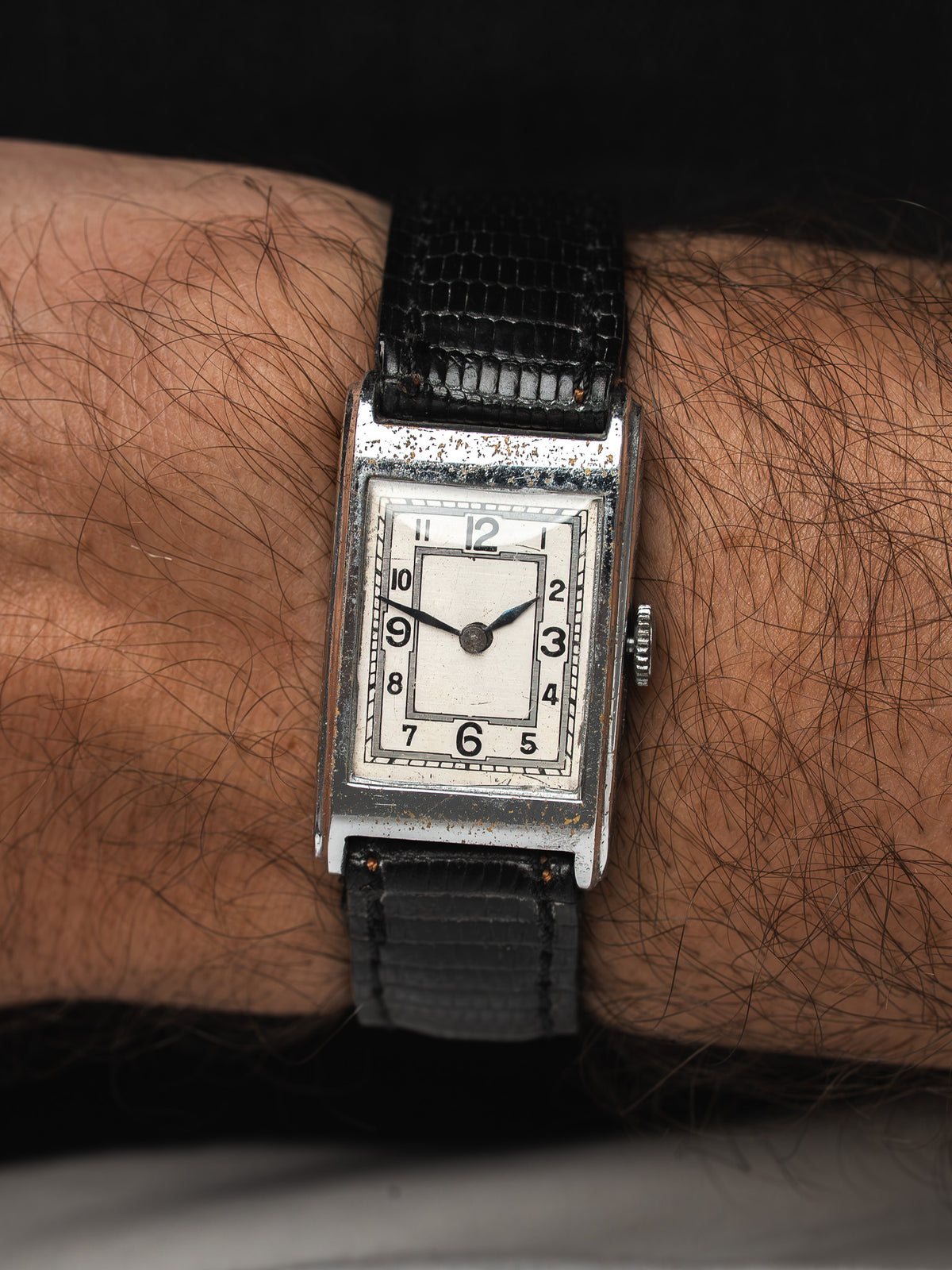 Montre vintage au boîtier rectangulaire argenté, cadran blanc et bracelet cuir noir au poignet
