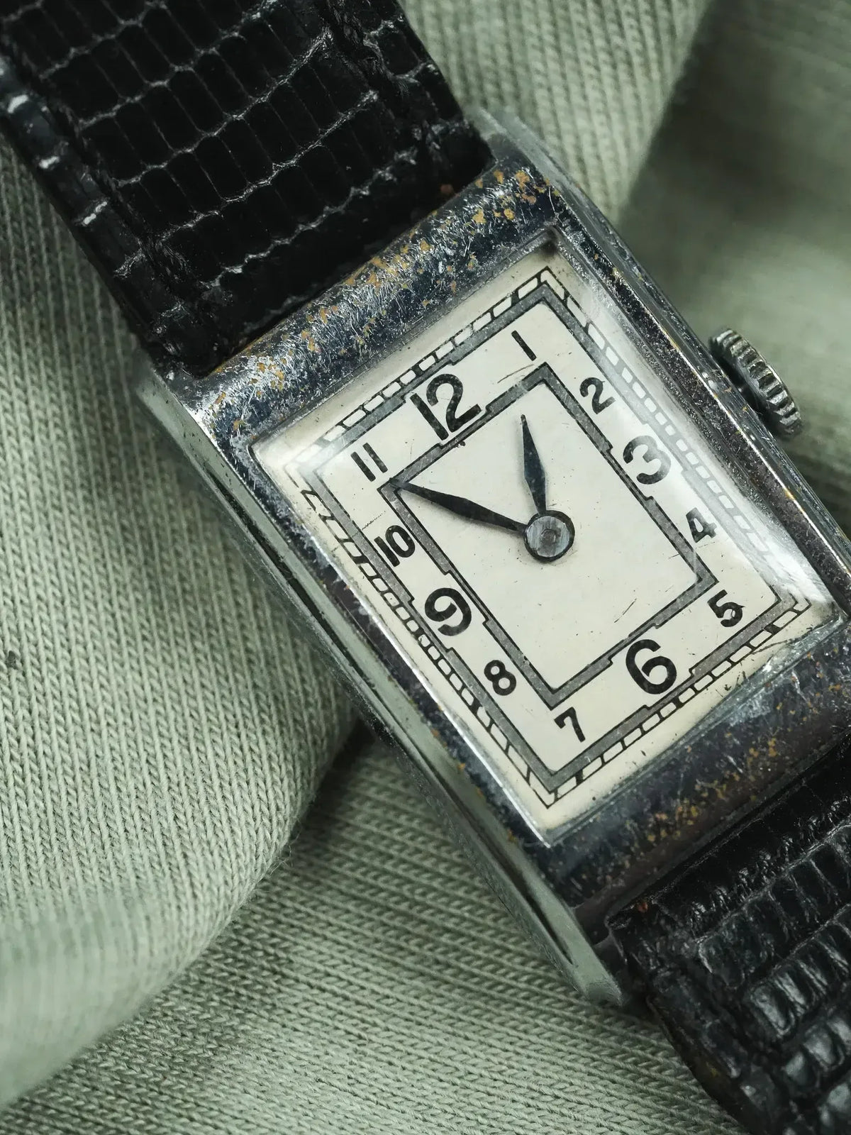 Vintage rectangular watch with white dial, black numerals, and textured black strap on fabric