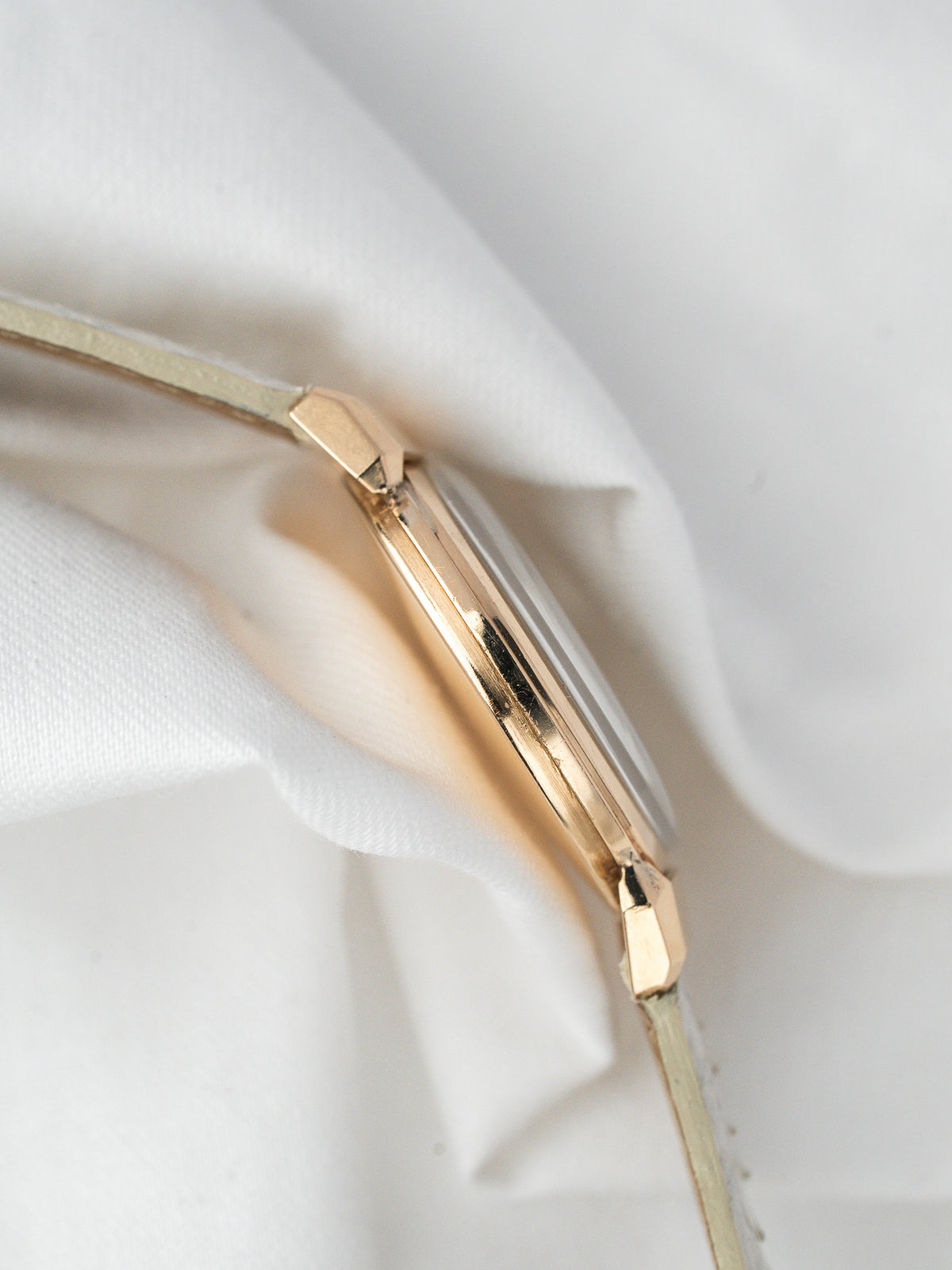 Vue de profil d'une montre vintage en or sur un tissu blanc froissé