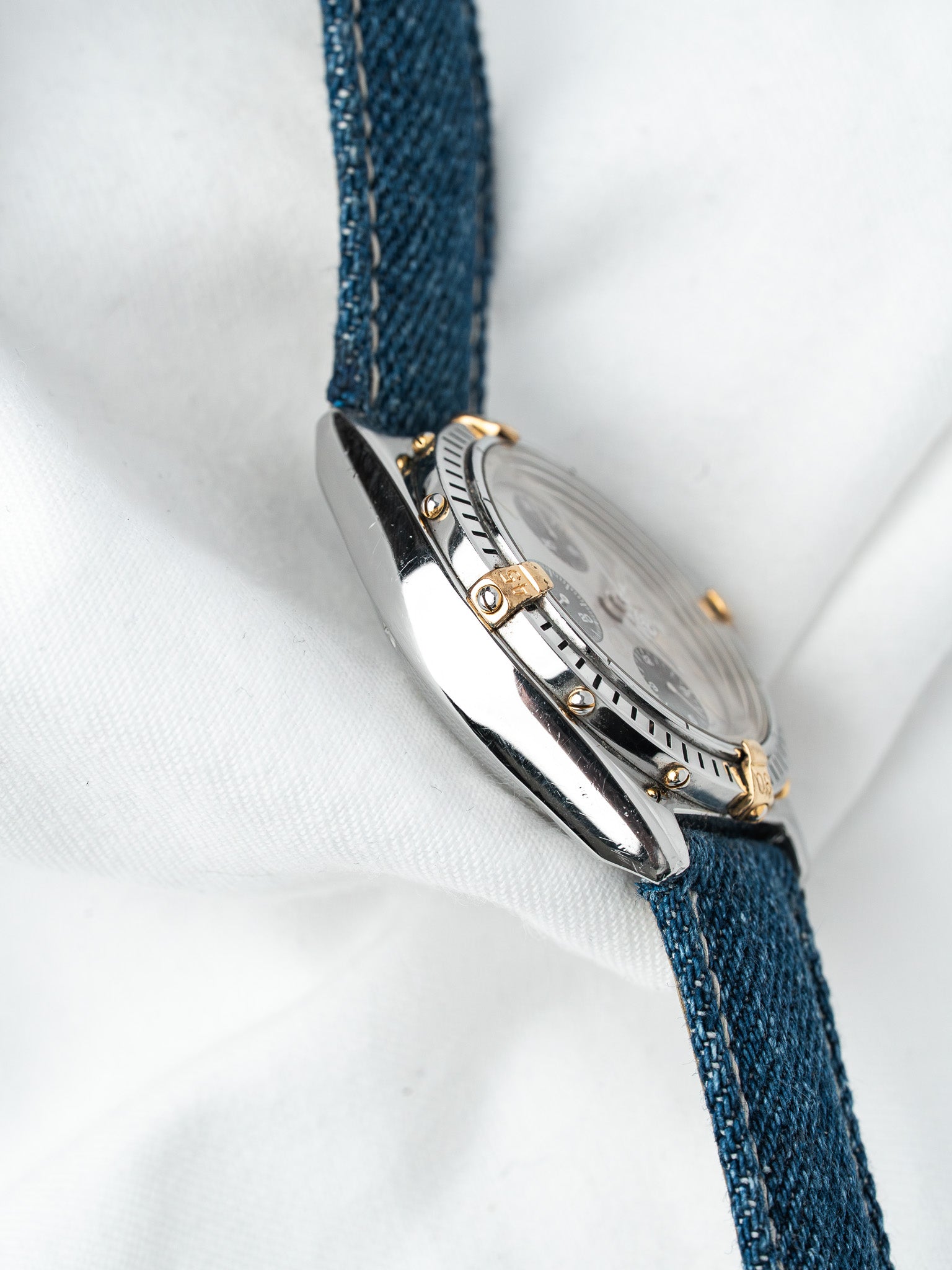 Vintage Omega Seamaster chronograph with steel case, gold accents, blue denim strap on white fabric