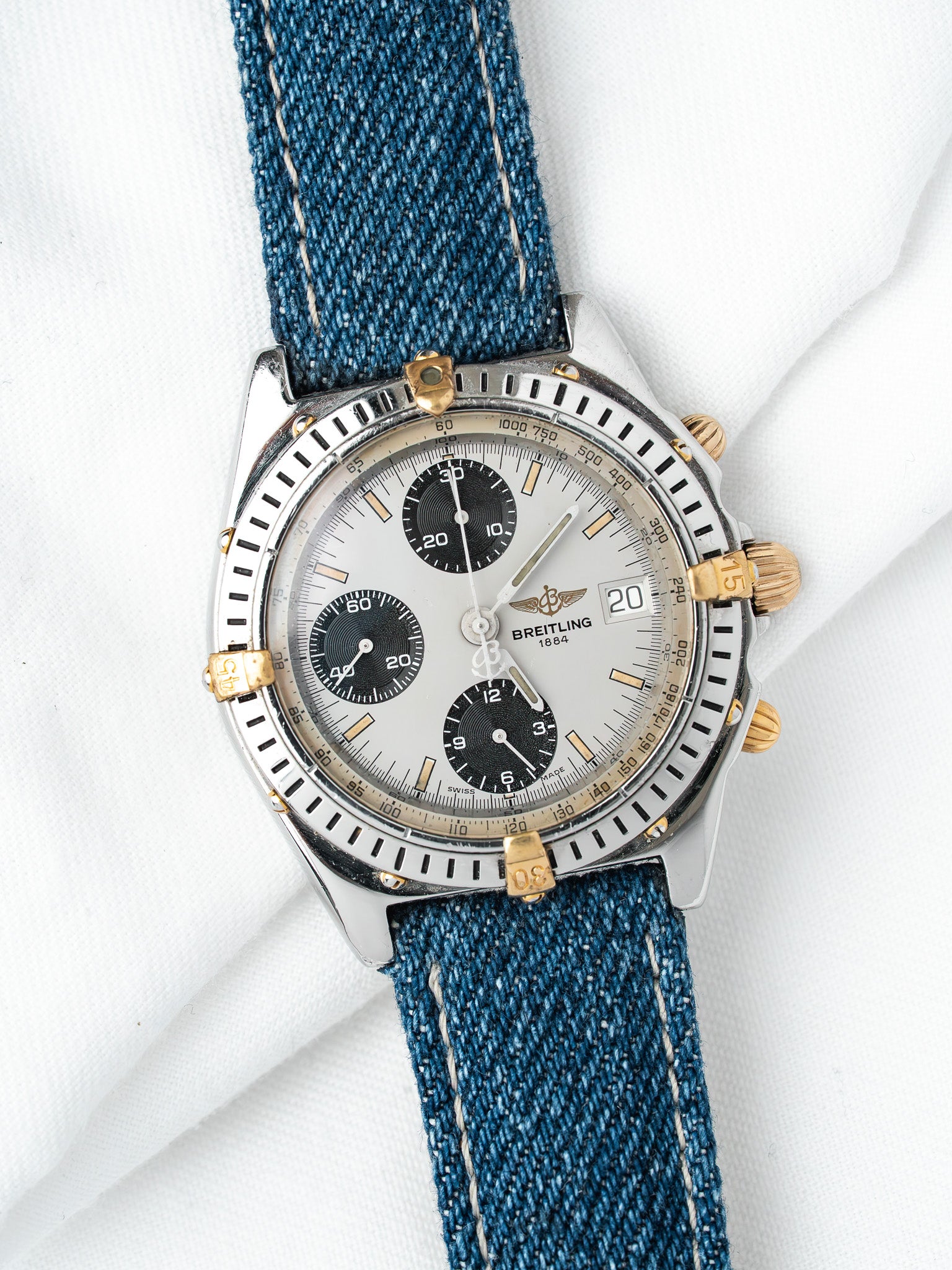 Breitling chronograph watch with silver dial, black subdials, and blue denim strap on white background