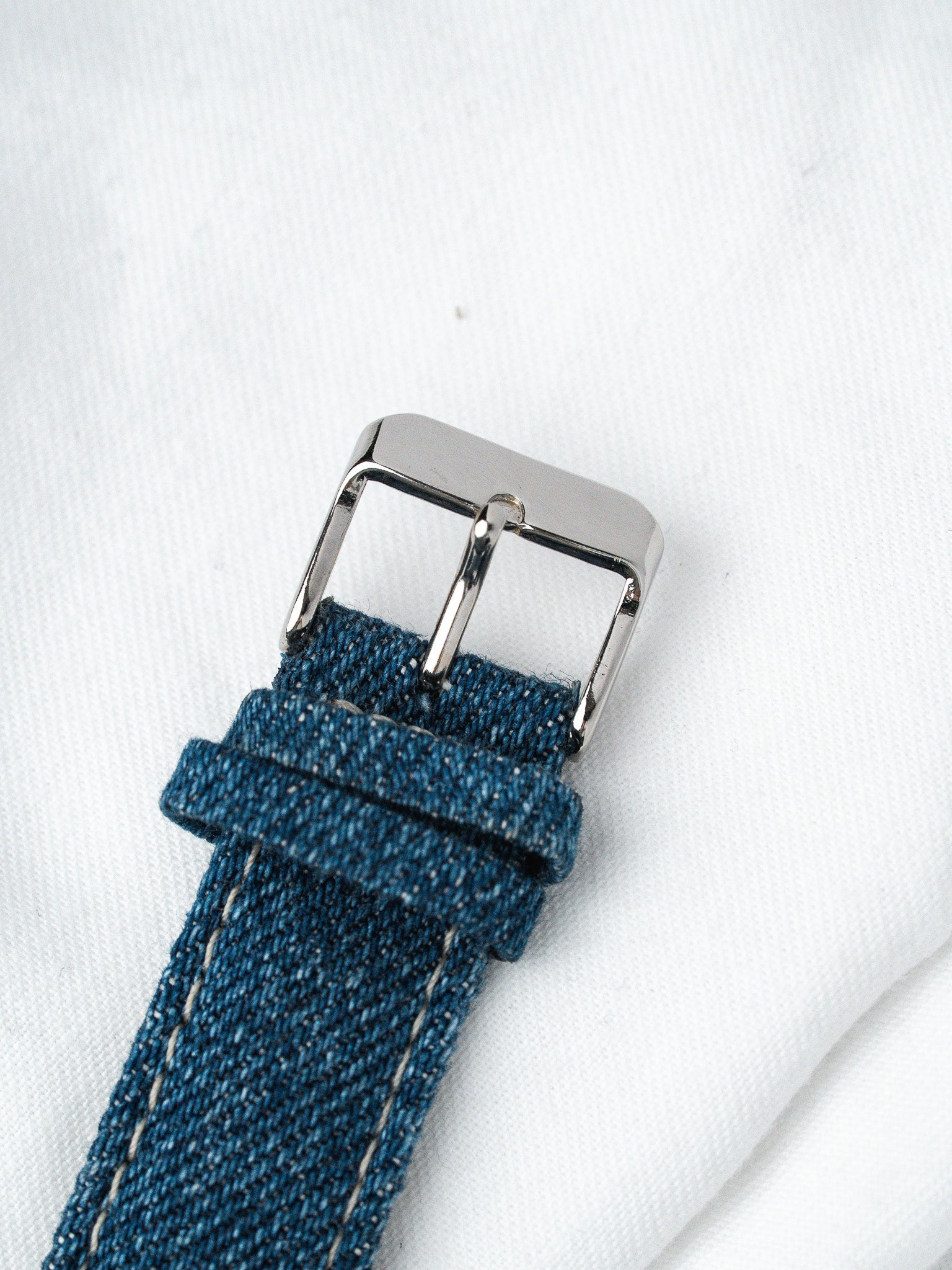 Blue denim watch strap with silver buckle on white fabric background