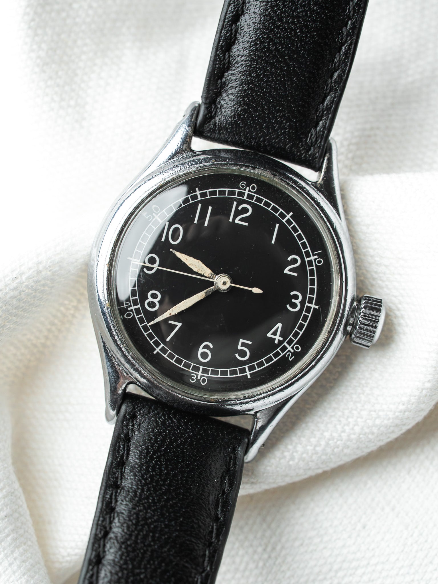 Vintage watch with black dial, white numerals, steel case, black leather strap on white fabric