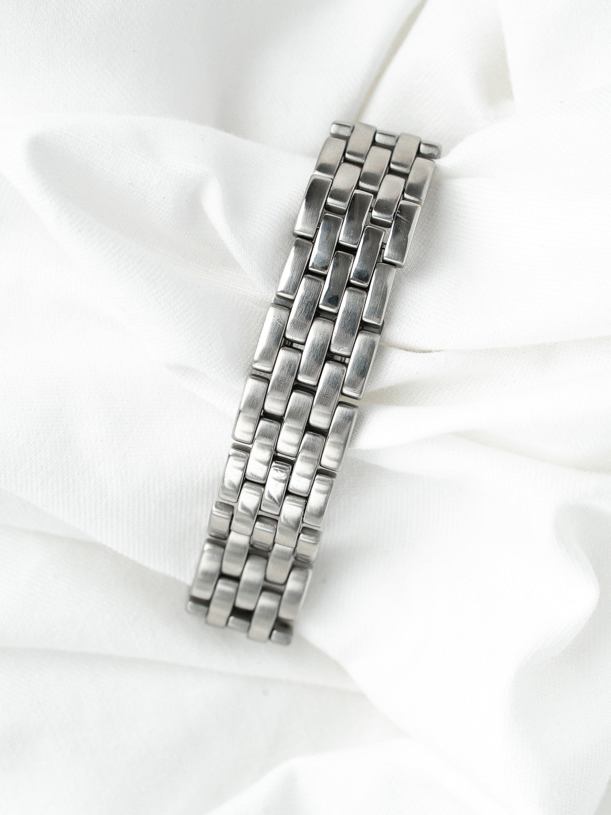 Bracelet de montre vintage en acier inoxydable argenté posé sur un tissu blanc