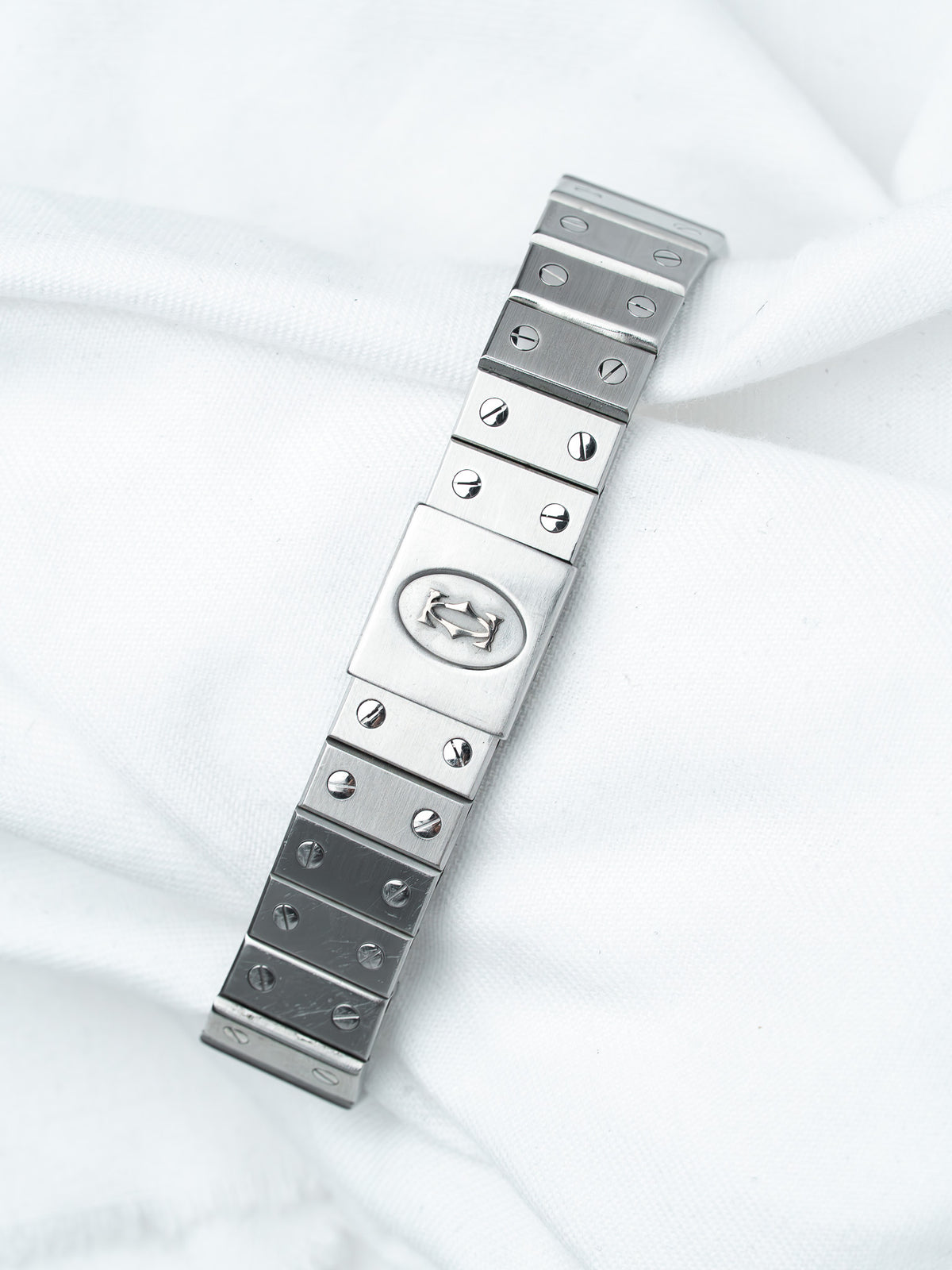 Stainless steel watch bracelet with screws and logo, displayed on white fabric