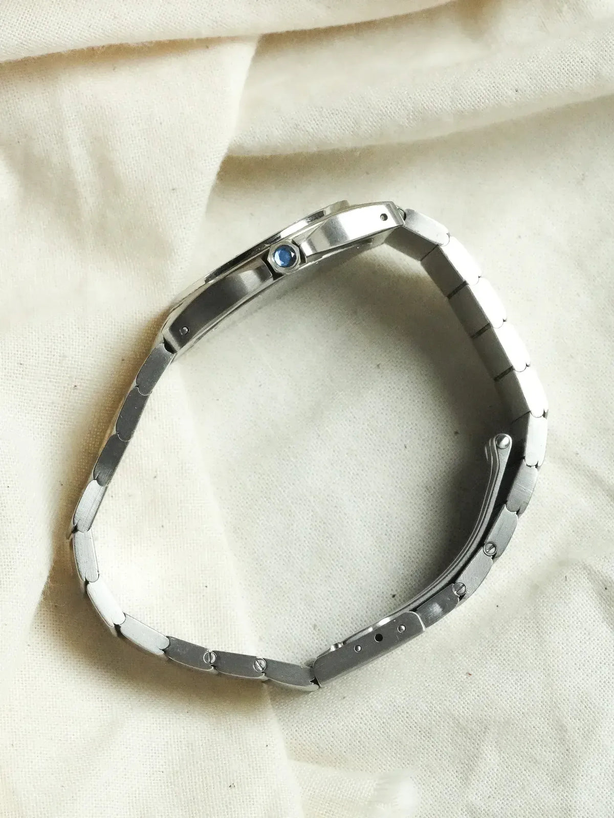 Cartier Santos vintage watch with steel bracelet and blue sapphire crown, on fabric background