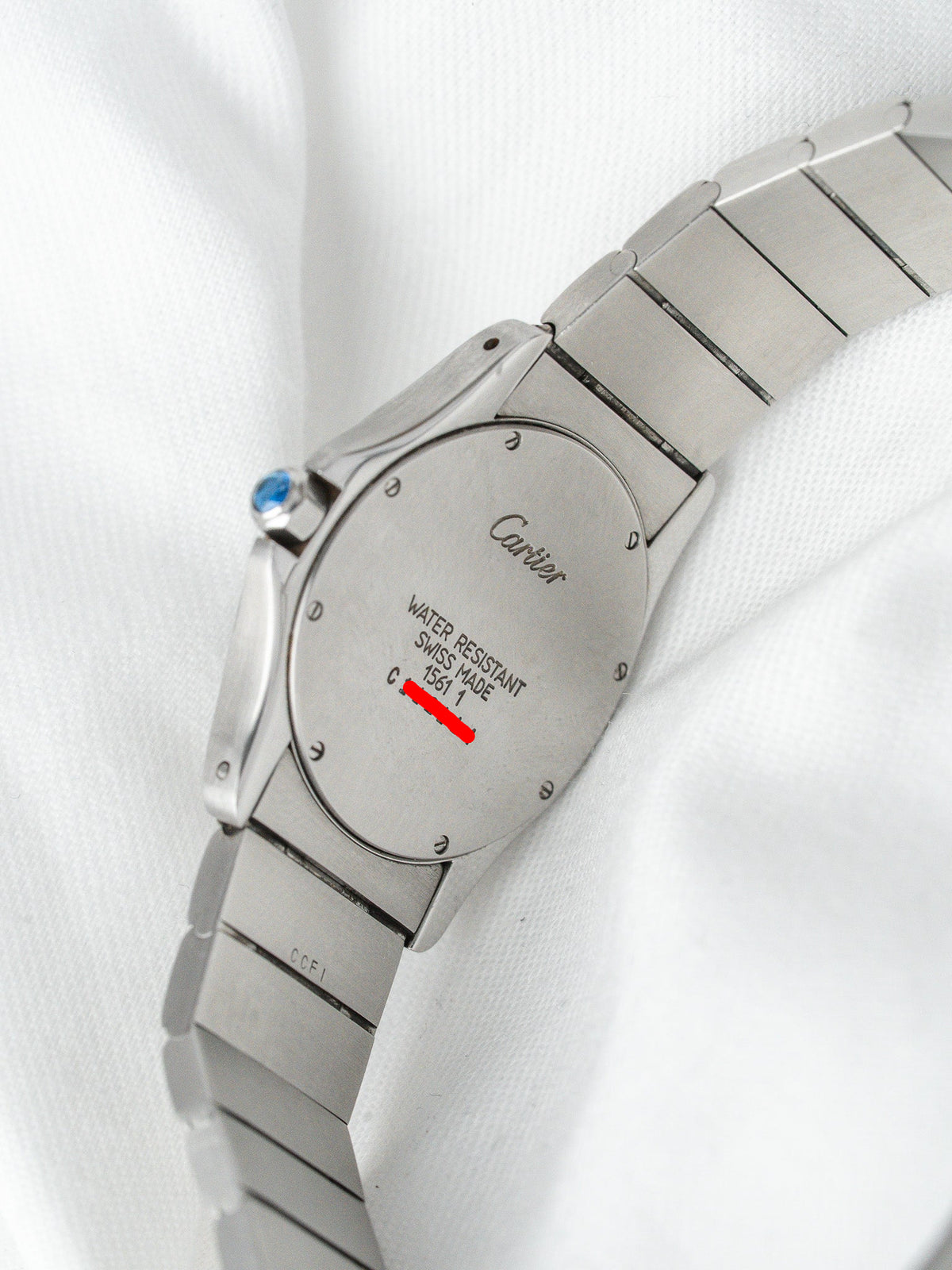 Cartier watch back with engraved logo, water resistant text, and blue crown on white fabric