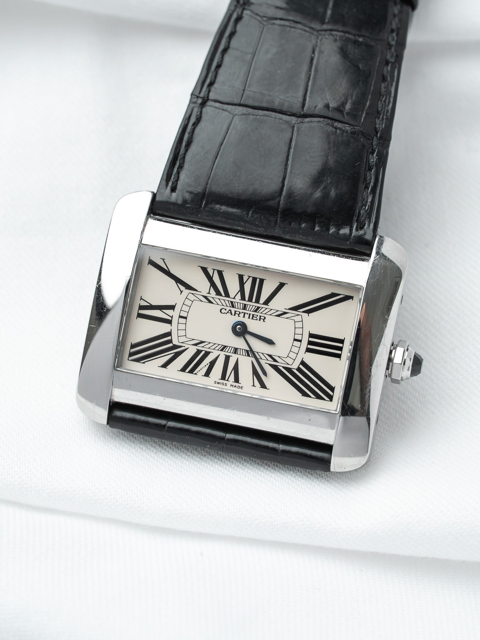 Cartier Tank watch with silver case, white dial, black Roman numerals, and black alligator strap