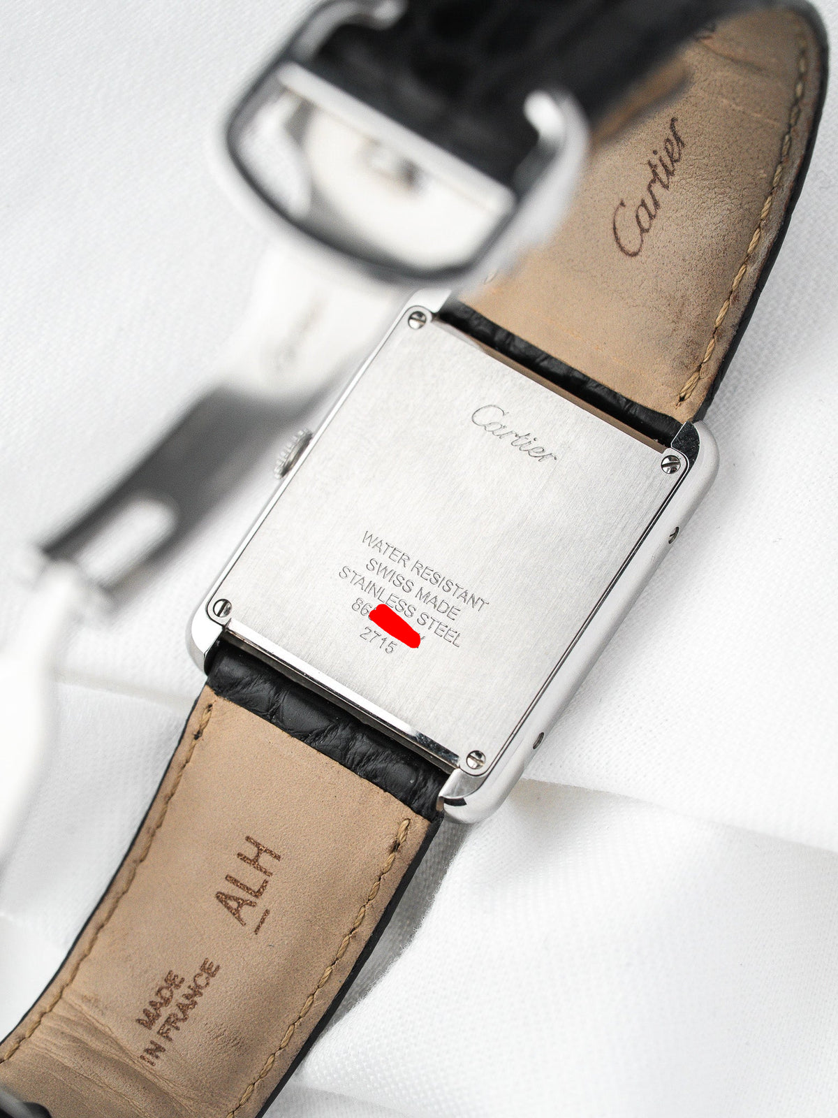 Dos d'une montre Cartier en acier avec bracelet en cuir noir sur fond blanc