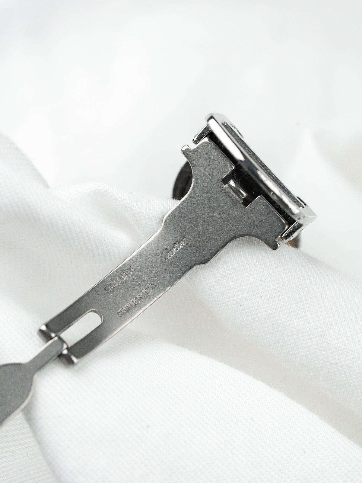 Fermoir de montre Cartier en acier inoxydable posé sur un tissu blanc