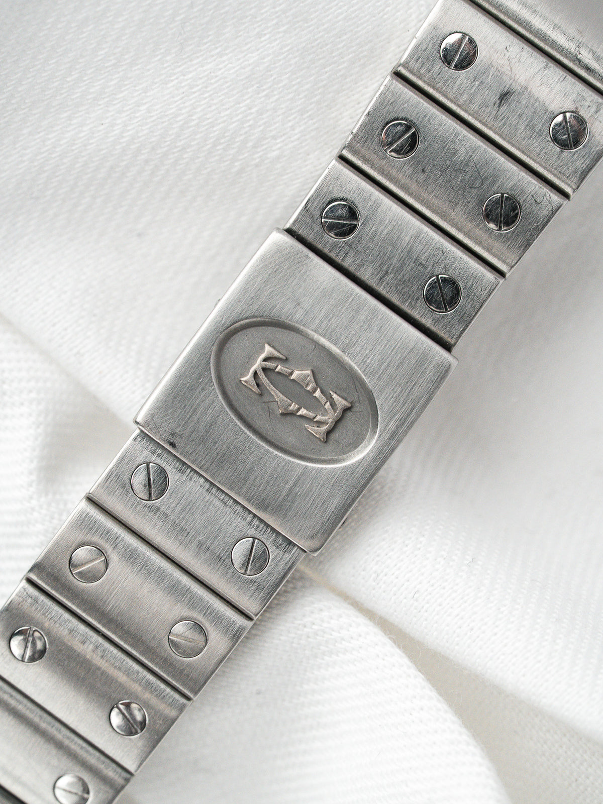 Bracelet de montre vintage en acier avec fermoir gravé d'un logo, sur fond blanc