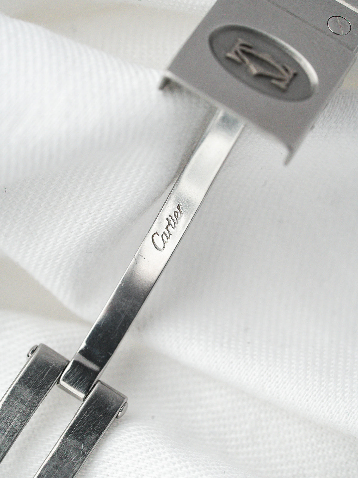 Détail du fermoir en acier d'une montre Cartier sur un tissu blanc