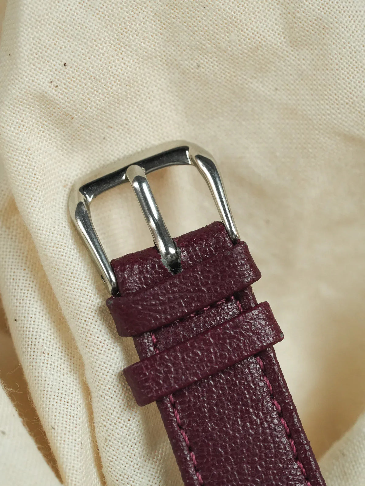Burgundy textured leather watch strap with silver buckle on canvas