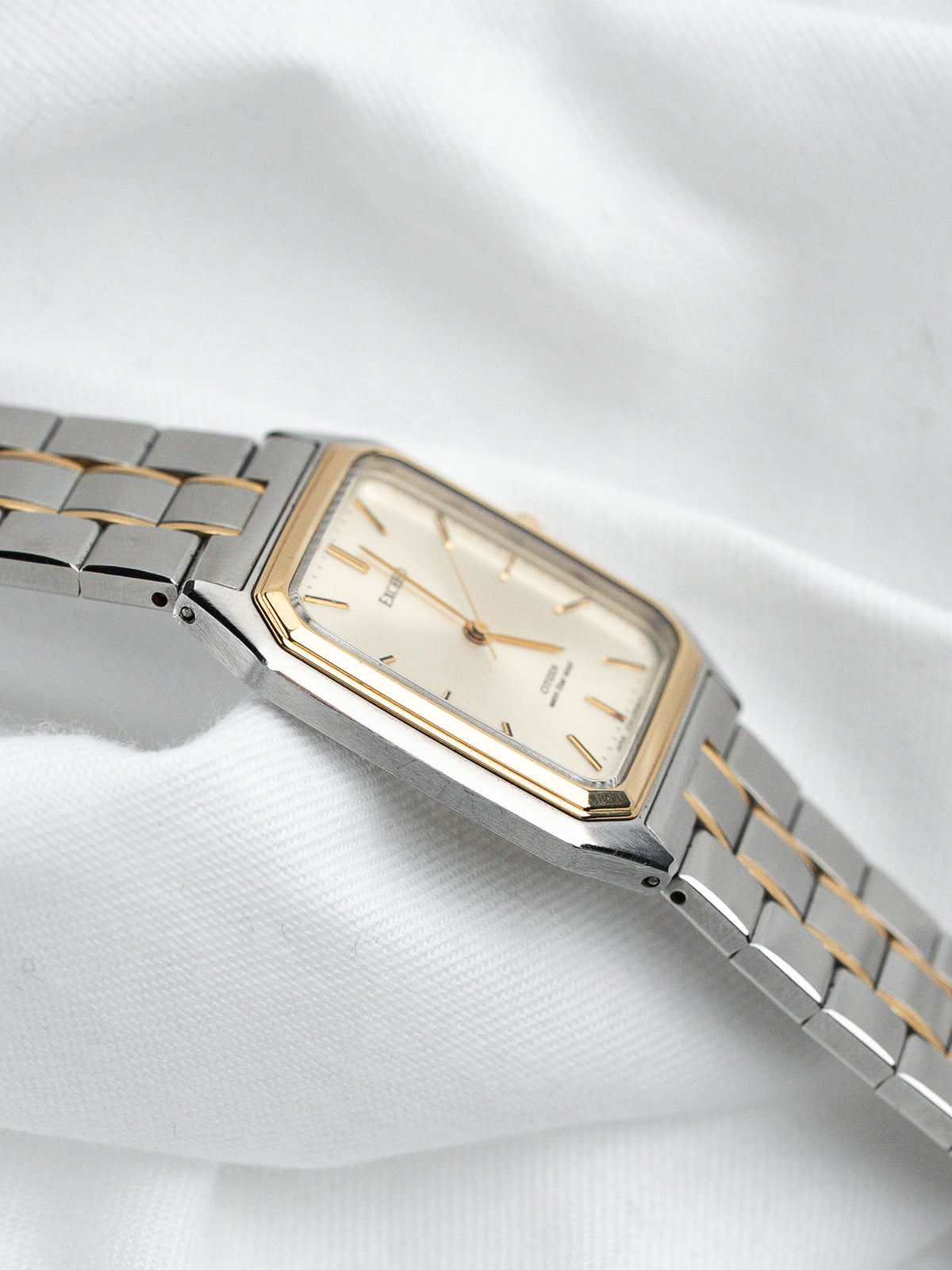 Montre vintage rectangulaire en acier et or avec bracelet articulé sur fond blanc.