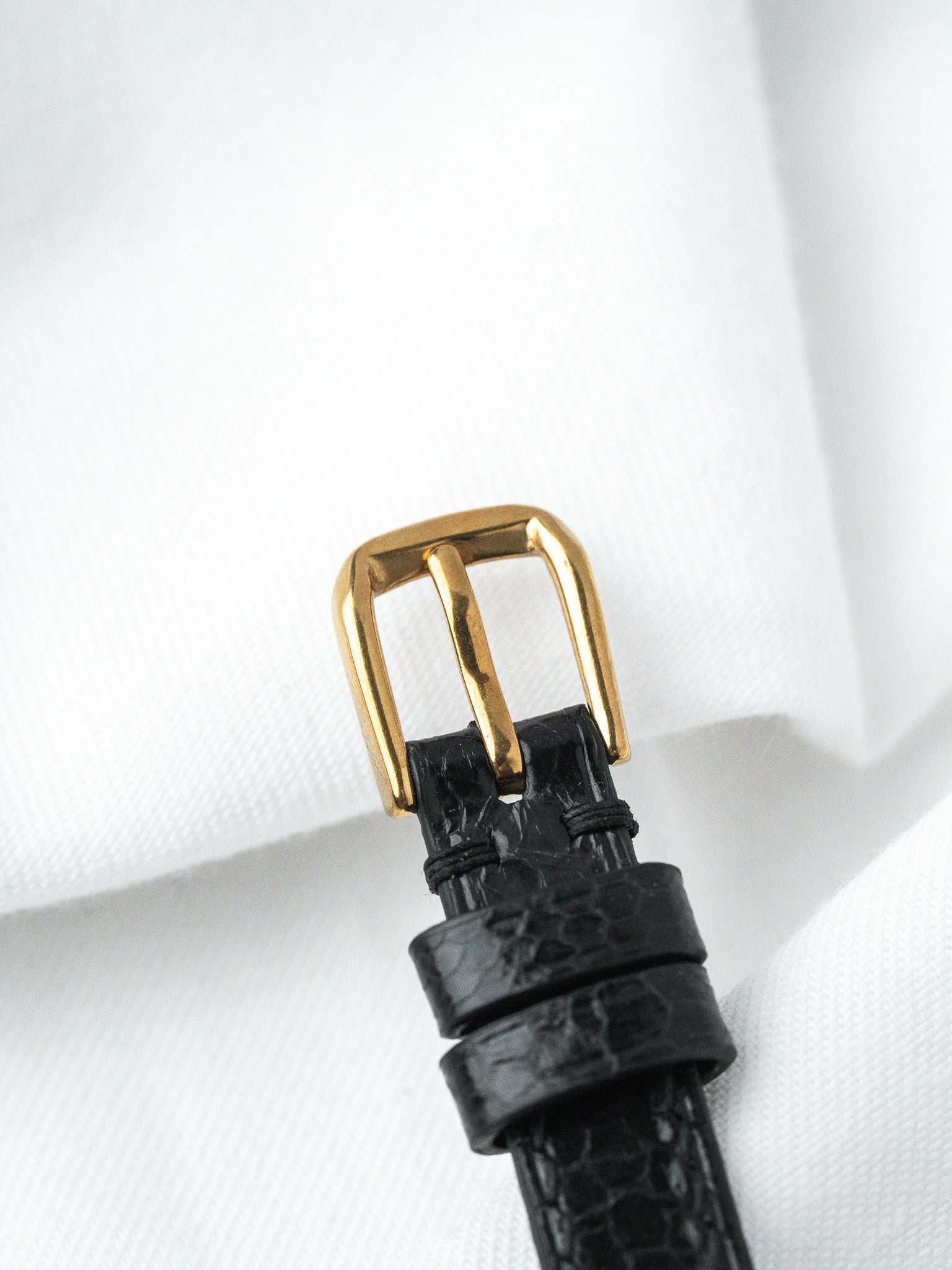 Black alligator leather watch strap with gold buckle on white fabric