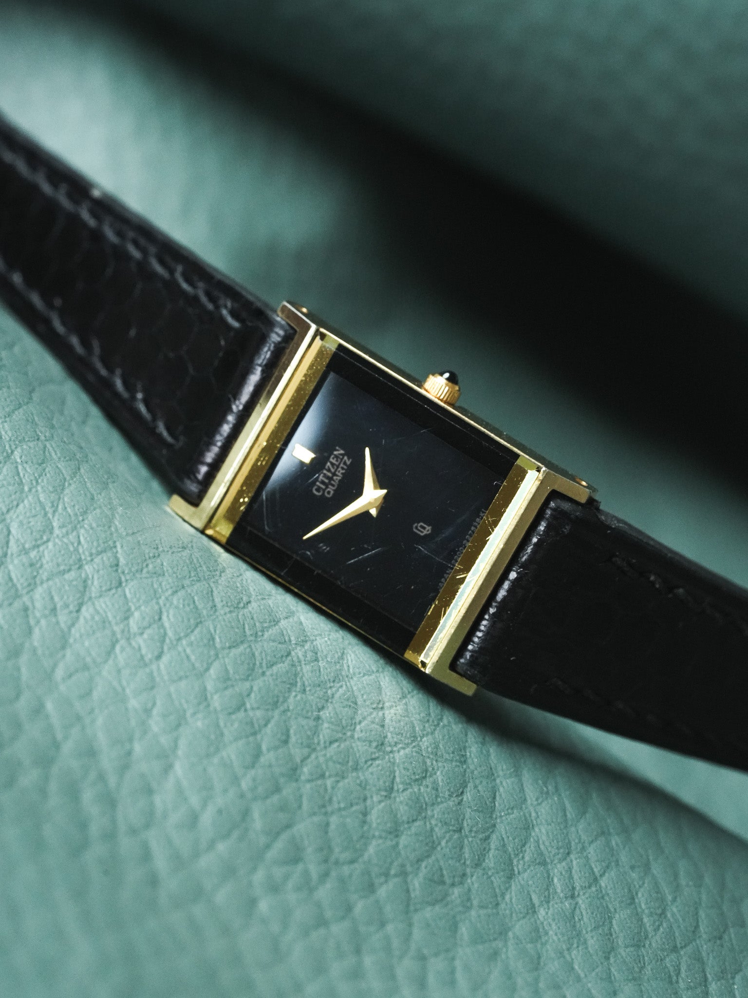 Citizen Quartz vintage watch with gold case, black dial, and leather strap on green texture