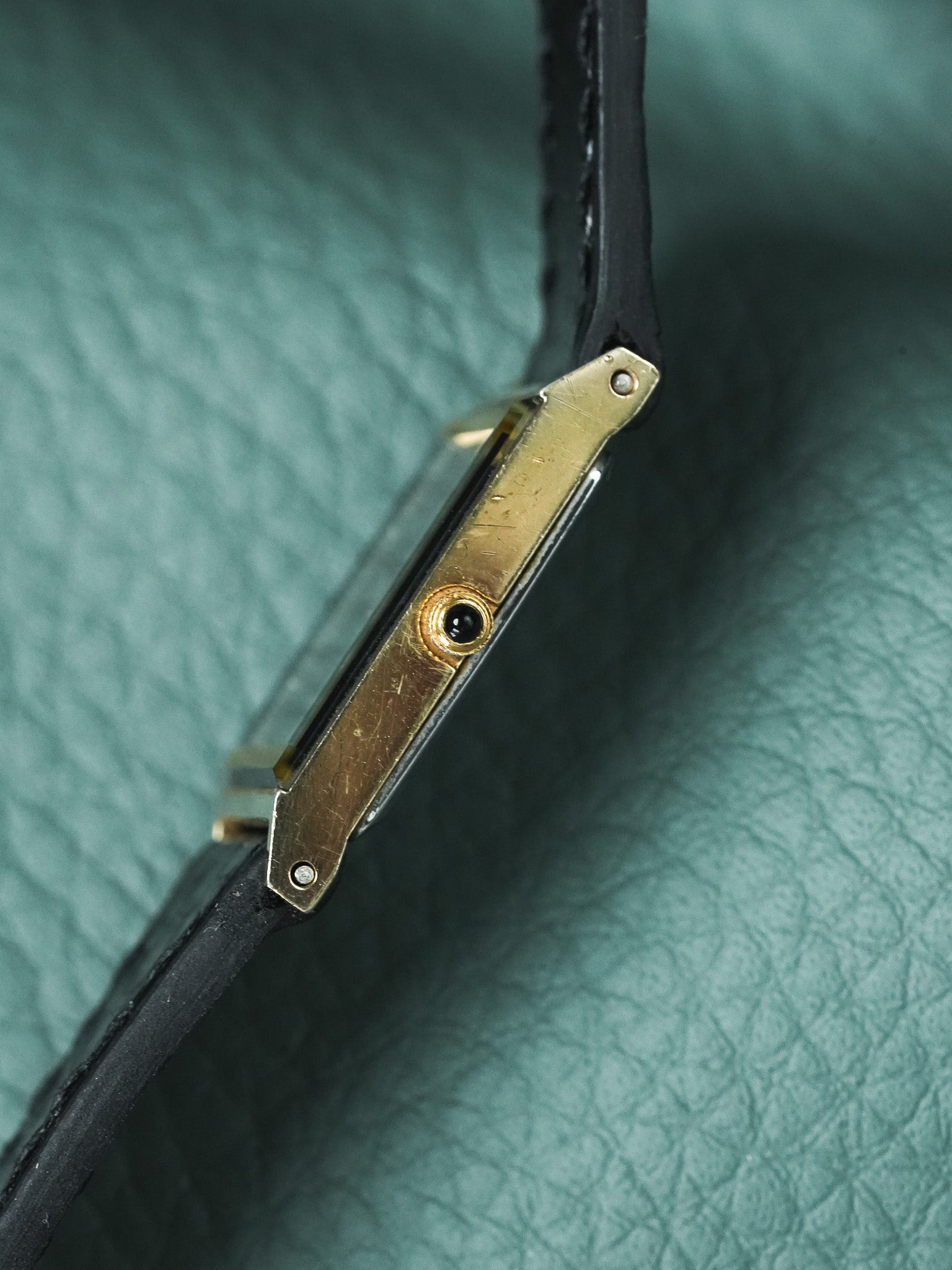 Vintage Cartier Tank watch with gold case and black leather strap on green leather