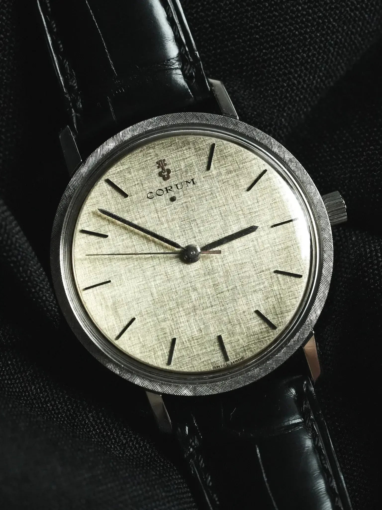 Corum vintage watch with textured silver dial, black leather strap, and brushed steel case