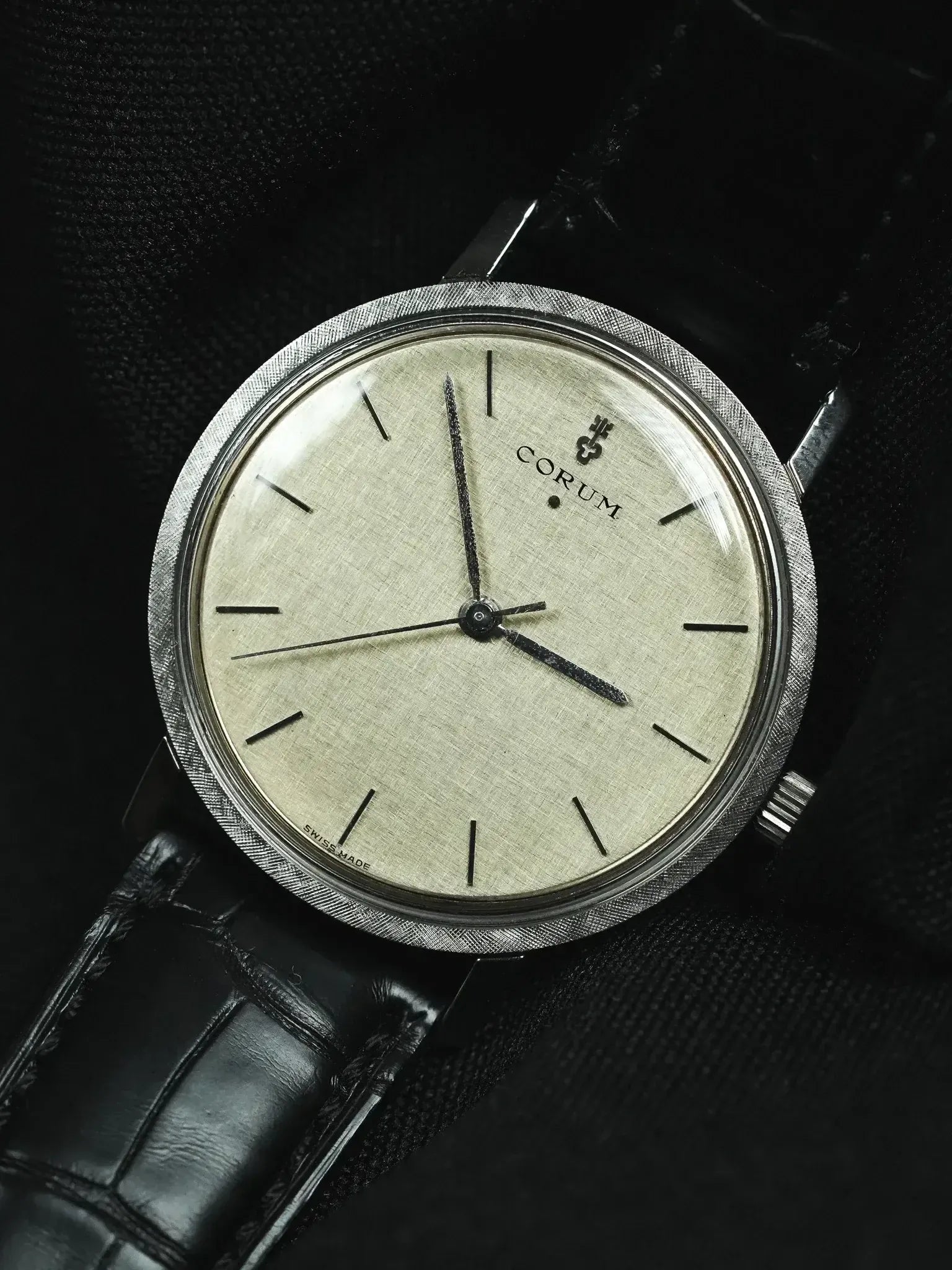 Vintage Corum watch with textured silver dial, black leather strap, and brushed steel case