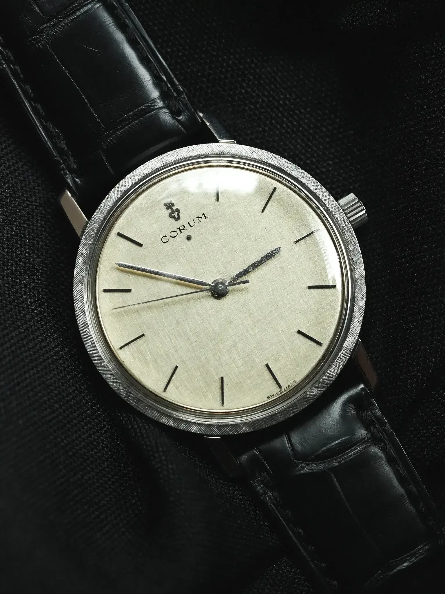 Vintage Corum watch with textured silver dial, black leather strap, and brushed steel case