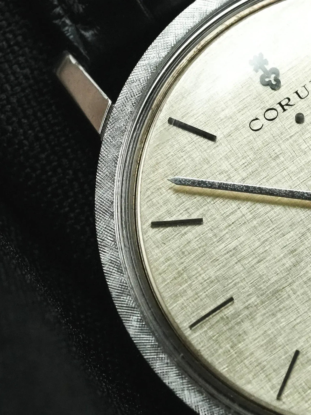 Vintage Corum watch with silvered linen dial, black baton markers, and black leather strap