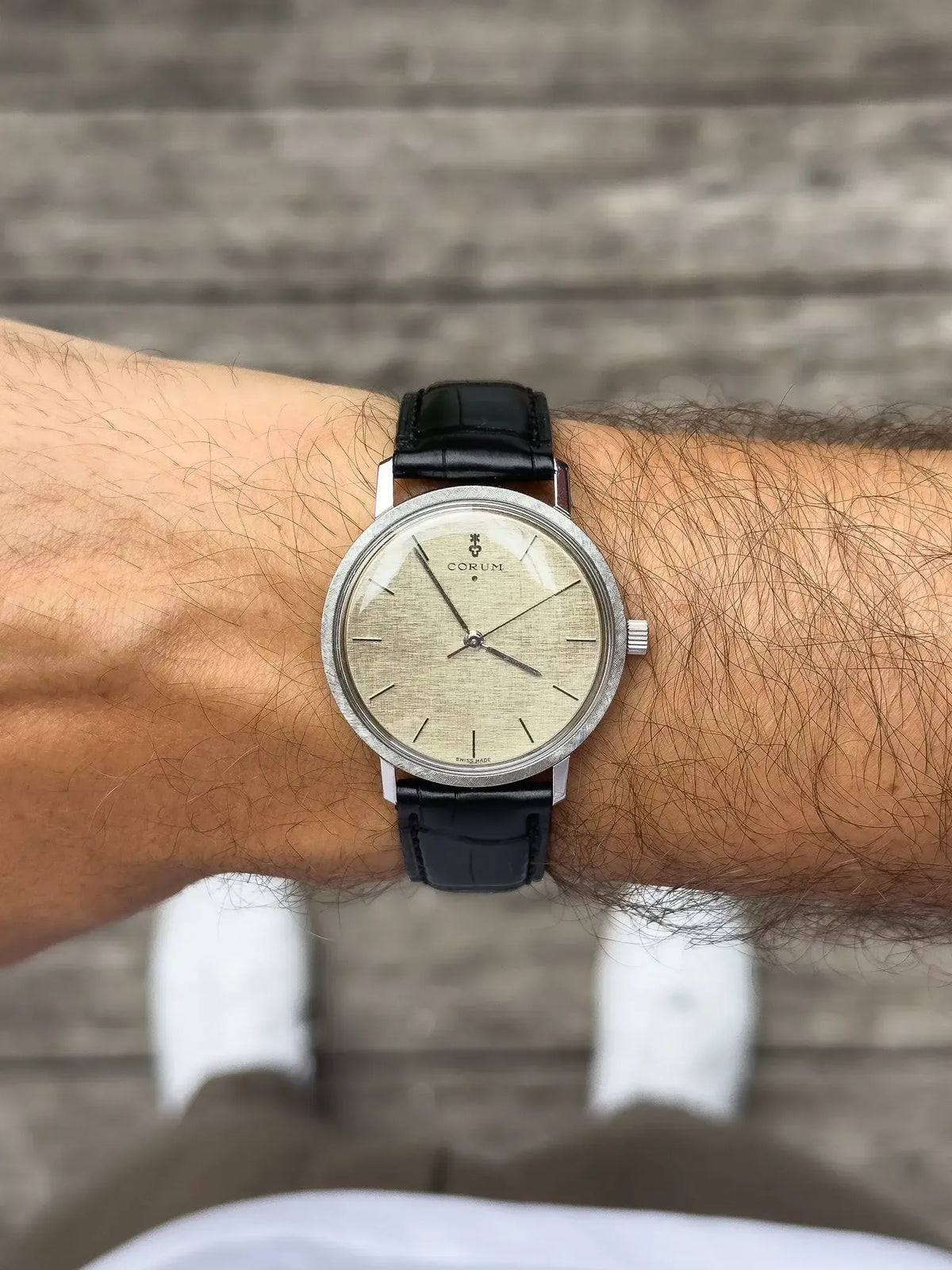 Corum vintage watch with silver case, cream dial, black leather strap on wrist