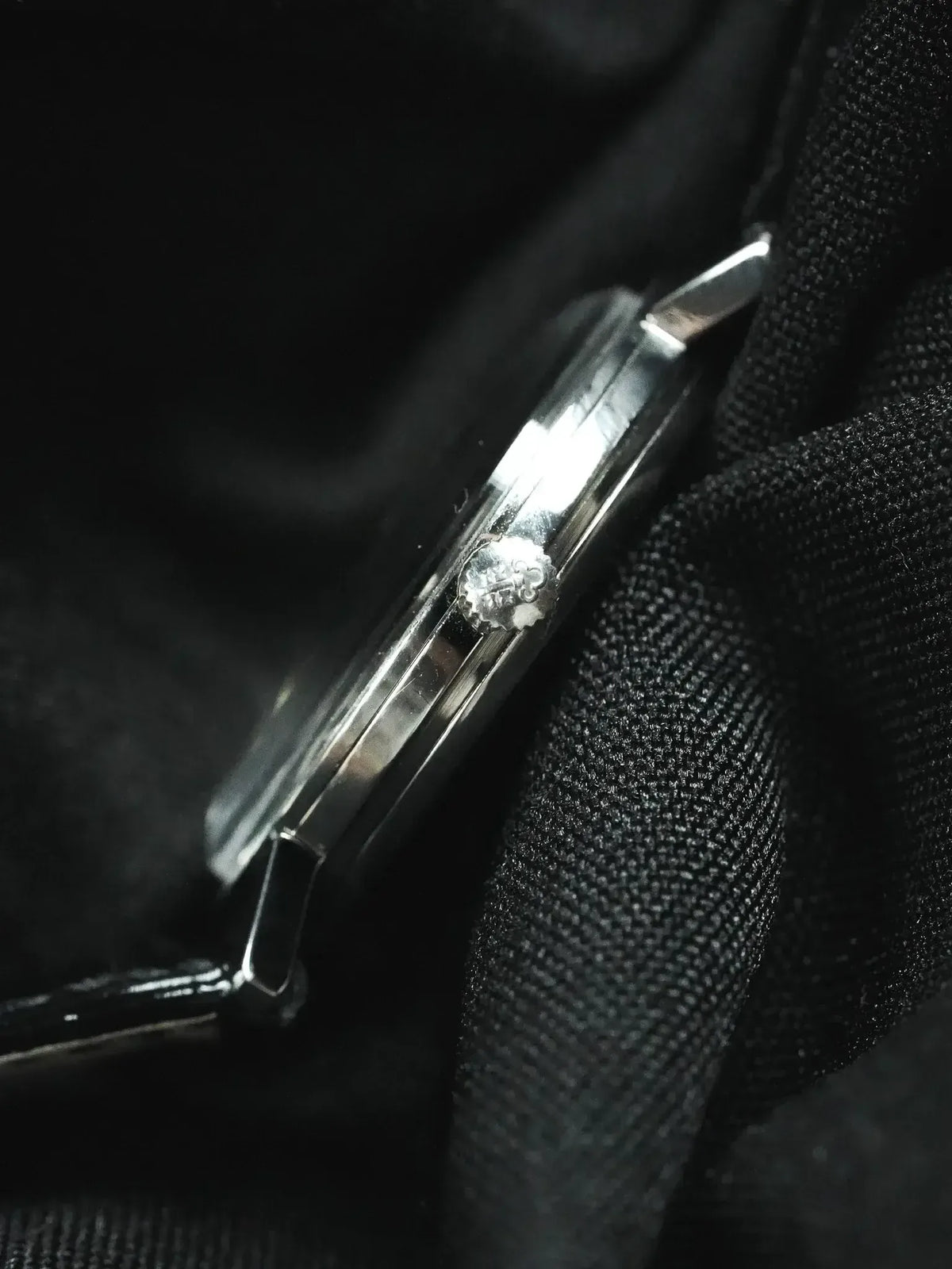 Cartier watch side view, polished steel case, crown with logo, on black fabric