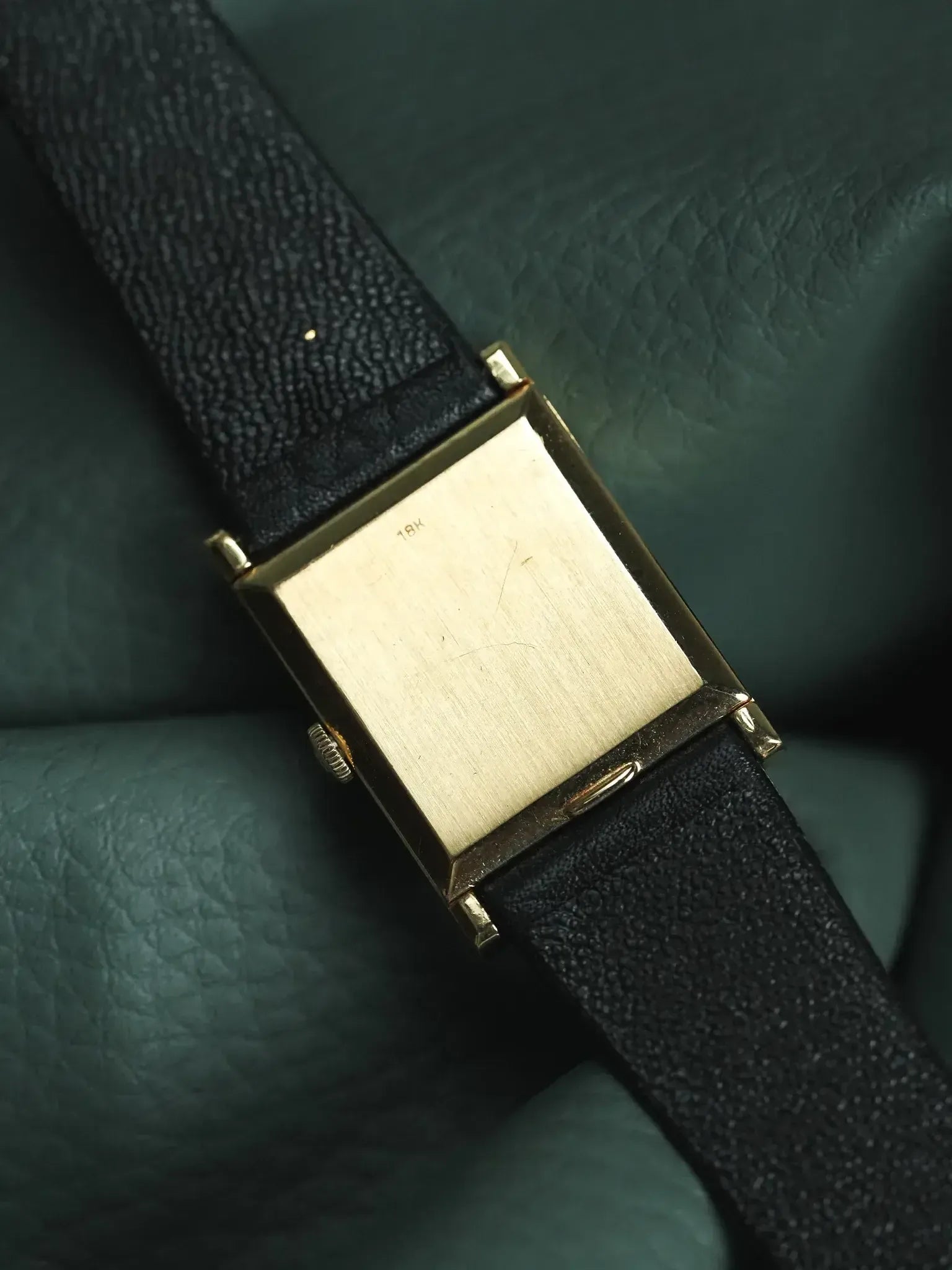 Vintage 18K gold rectangular watch case with black textured strap on green leather