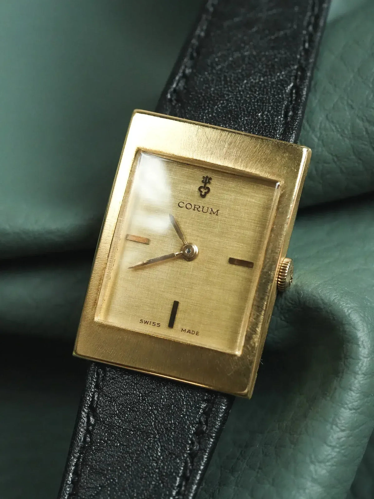 Vintage Corum watch with gold rectangular case, black leather strap, and minimalist dial