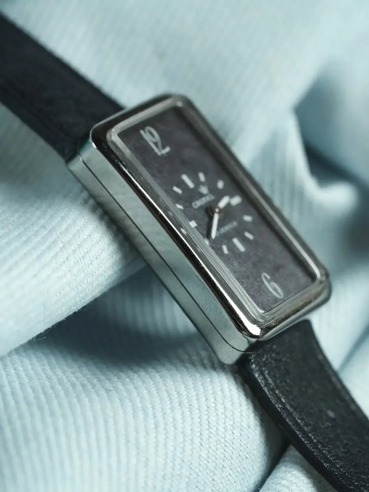Cartier rectangular watch with black dial, silver case, and black leather strap