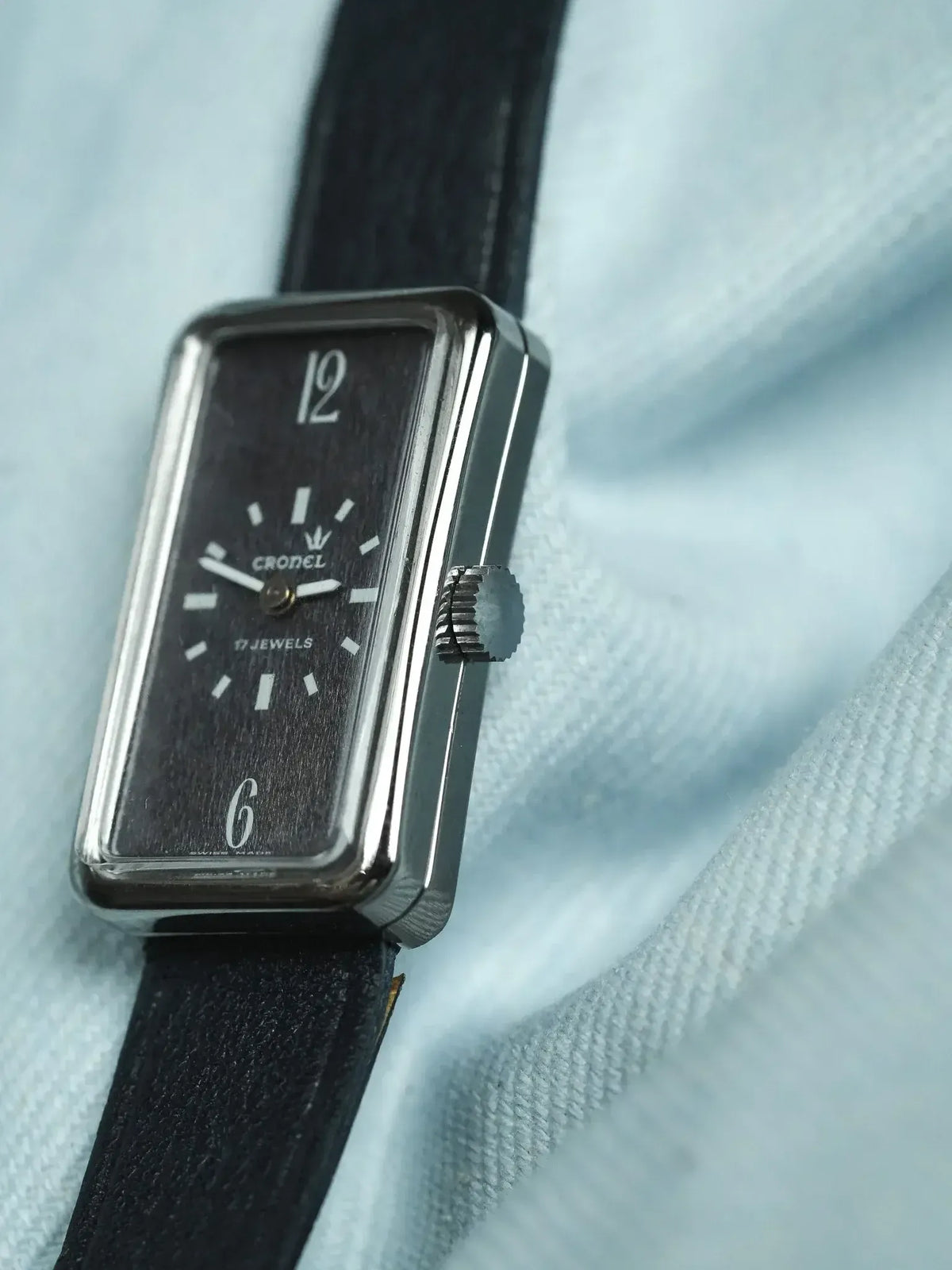 Cronel vintage watch with black dial, white markers, and black leather strap on fabric