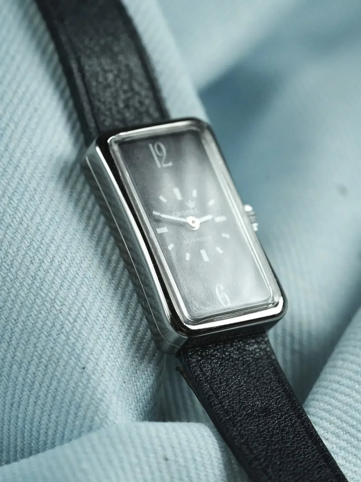 Montre Universal Genève vintage, boîtier rectangulaire acier, cadran gris, bracelet cuir noir