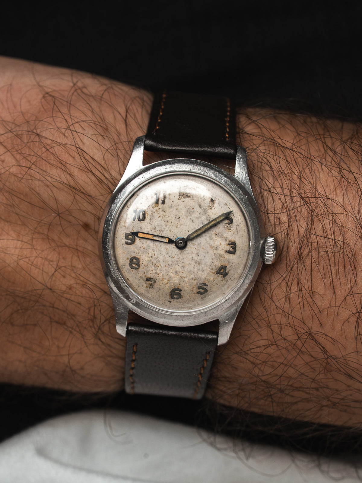 Montre vintage en acier au cadran patiné et bracelet cuir noir, portée au poignet