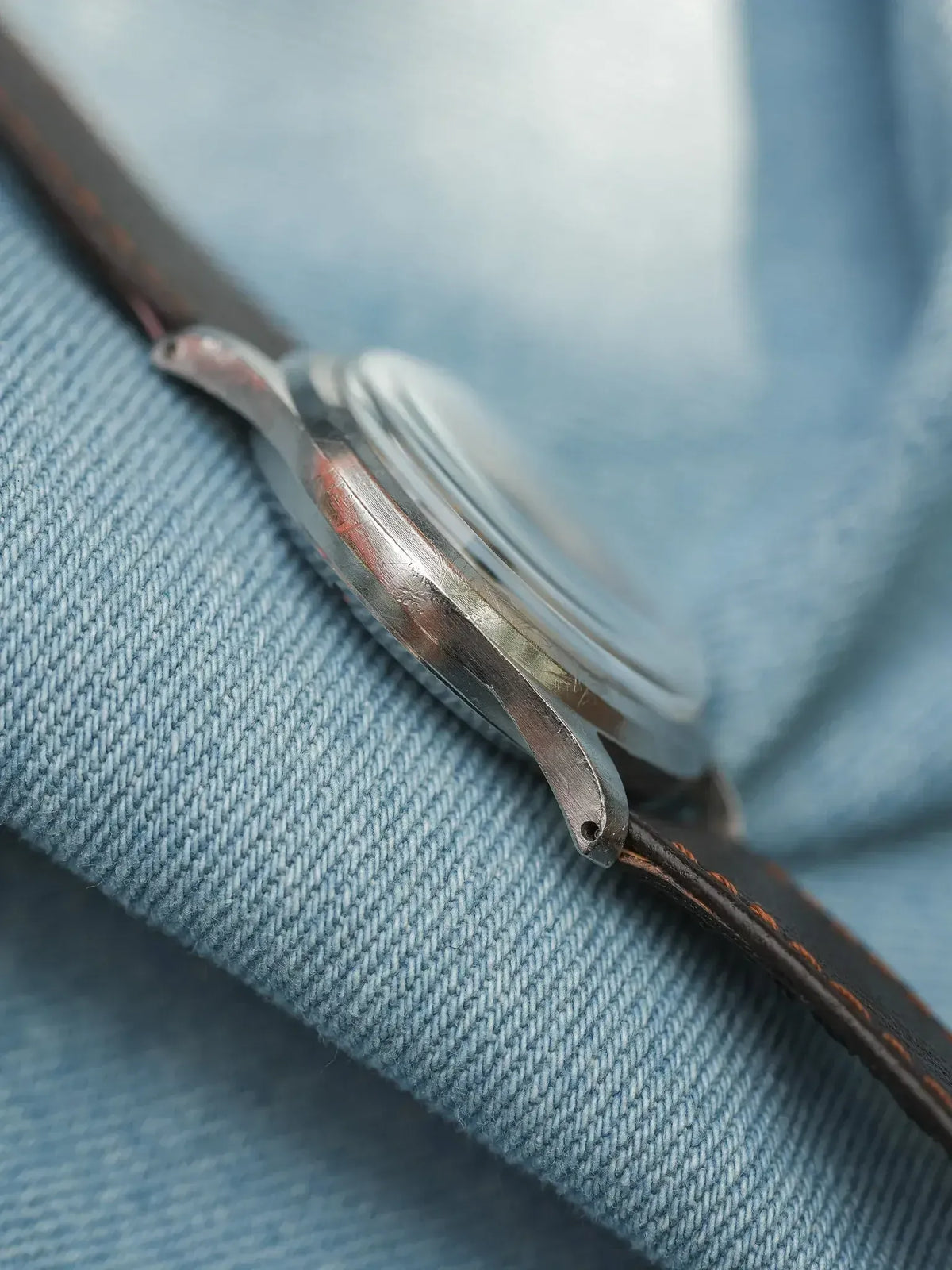 Vintage watch with steel case and brown leather strap on denim