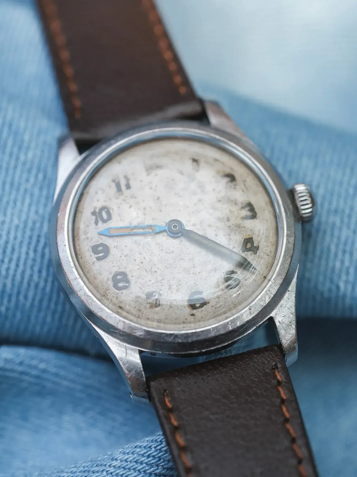 Vintage wristwatch with aged dial, steel case, brown leather strap on denim