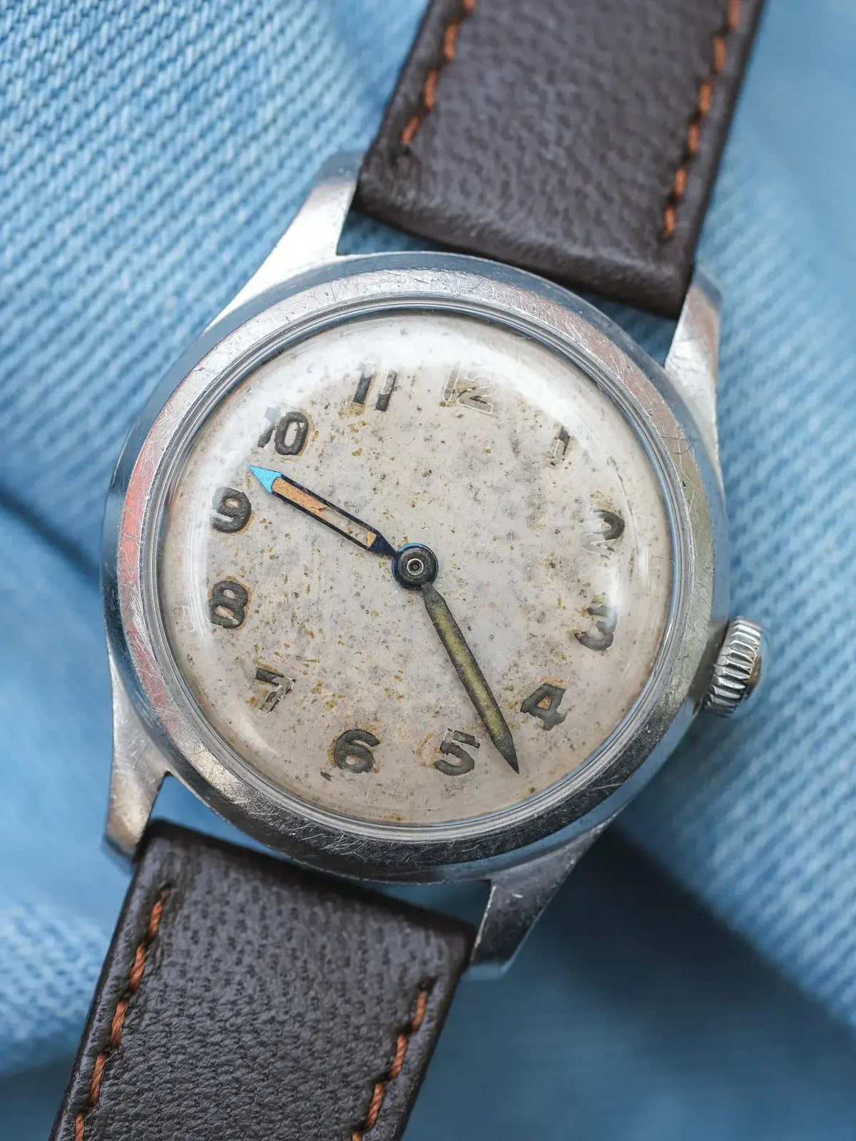 Vintage wristwatch with aged dial, steel case, brown leather strap on denim