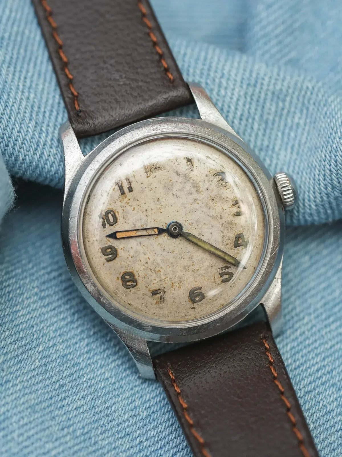 Vintage wristwatch with aged dial, steel case, brown leather strap on denim