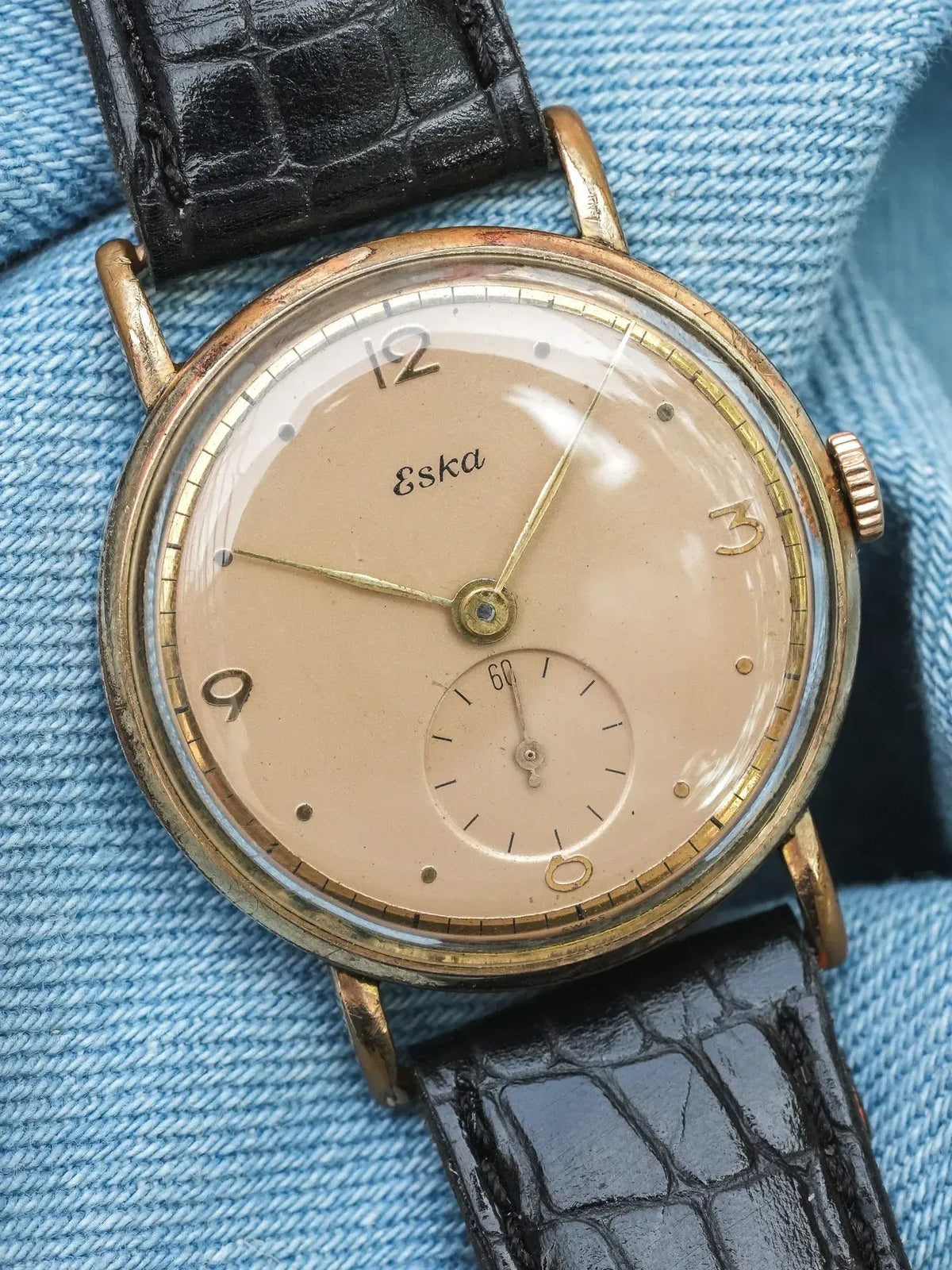 Vintage Eska watch with beige dial, gold hands, black crocodile strap on denim