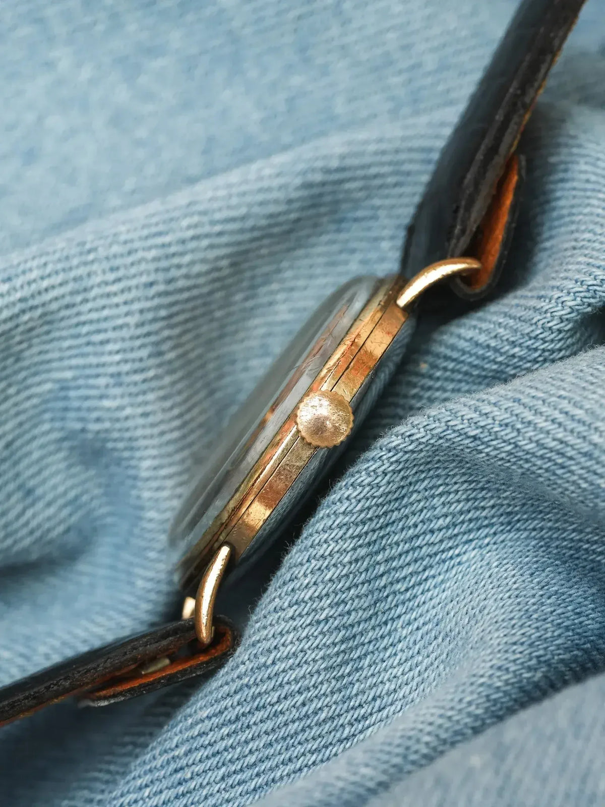 Vintage watch with gold-toned case and black leather strap on denim
